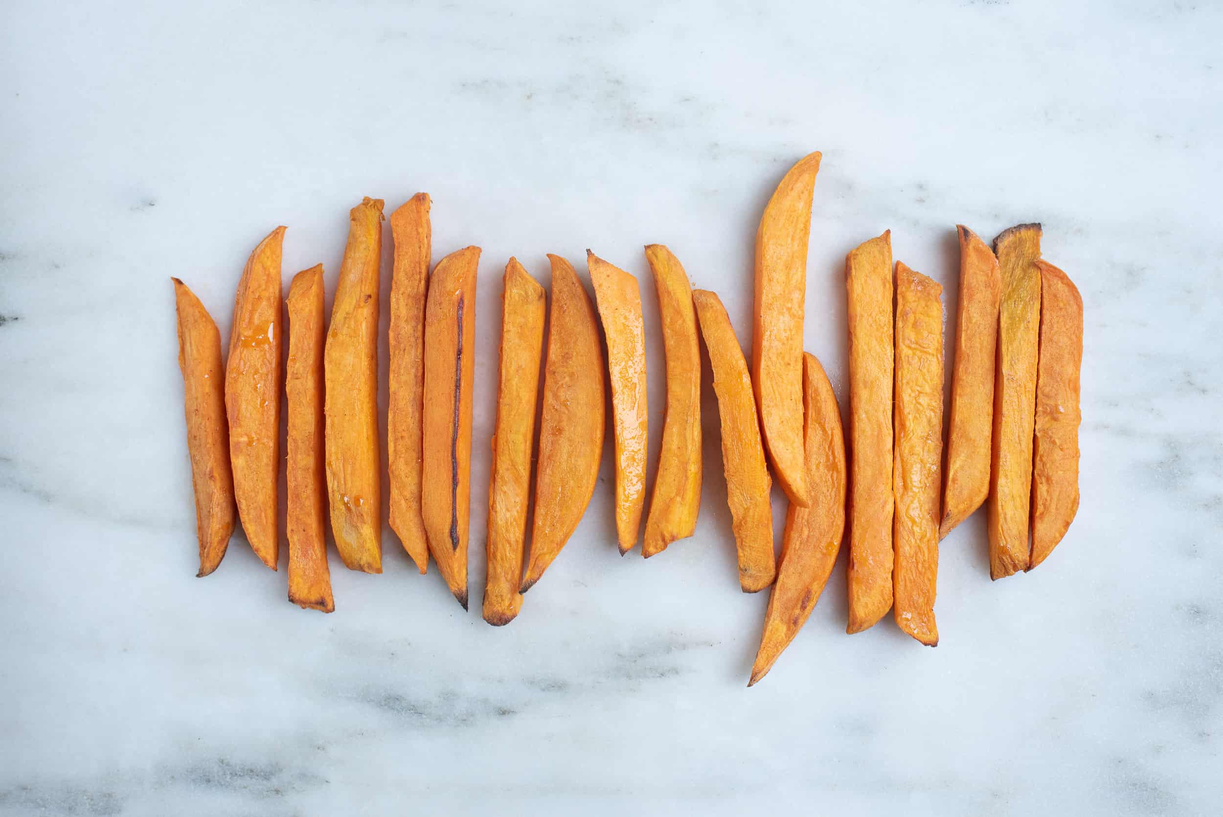 row of peeled, baked sweet potato fries lined up on countertop