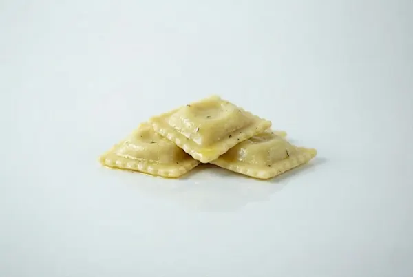 Ravioli for babies Three golden brown ravioli pieces are stacked neatly against a white background. The pasta is sprinkled with black pepper, creating a simple, elegant presentation.