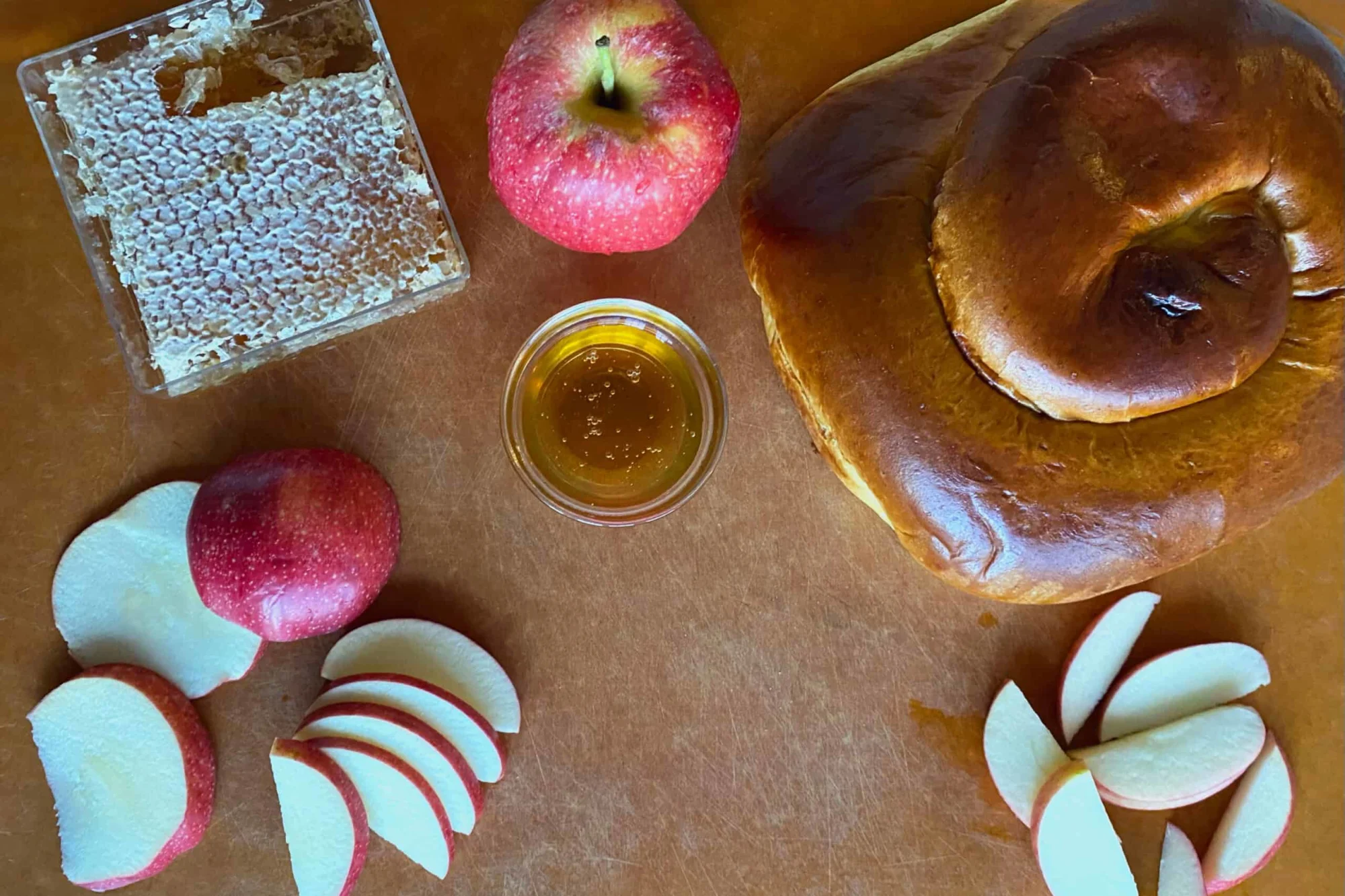 a cutting board with challah, apples and honey on it