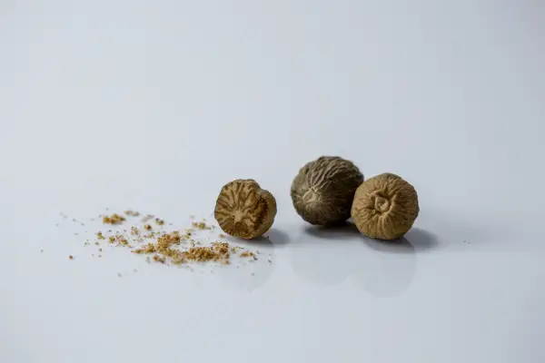 three whole nutmegs next to a little bit of finely ground nutmeg on a white background