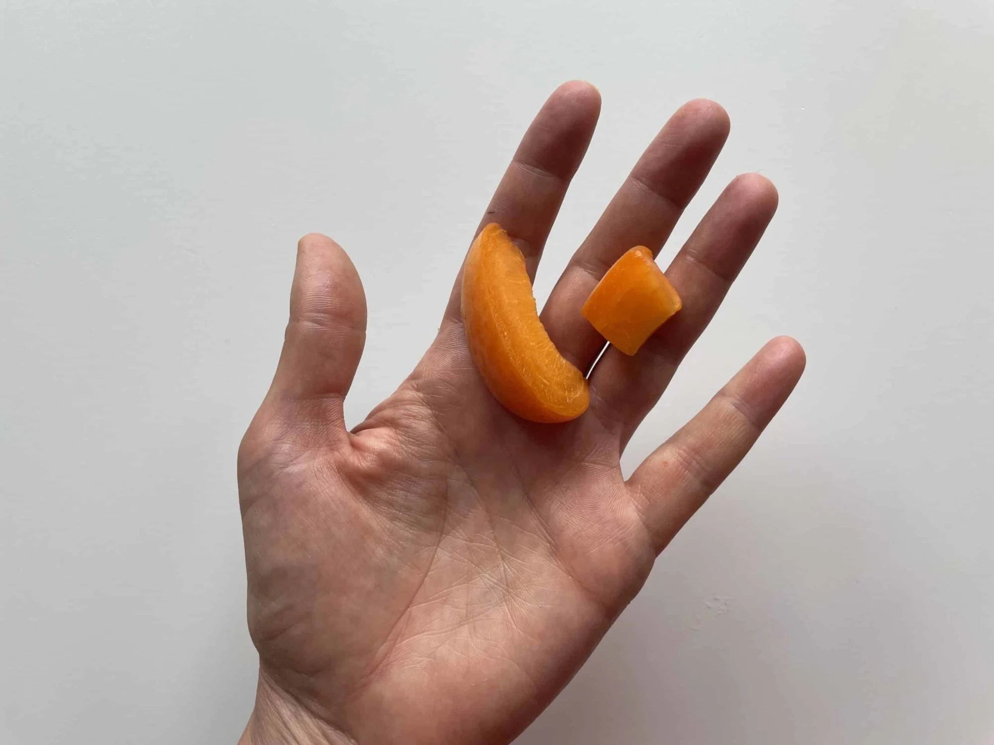 a hand holding one slice and one bite-sized pieces of ripe apricot