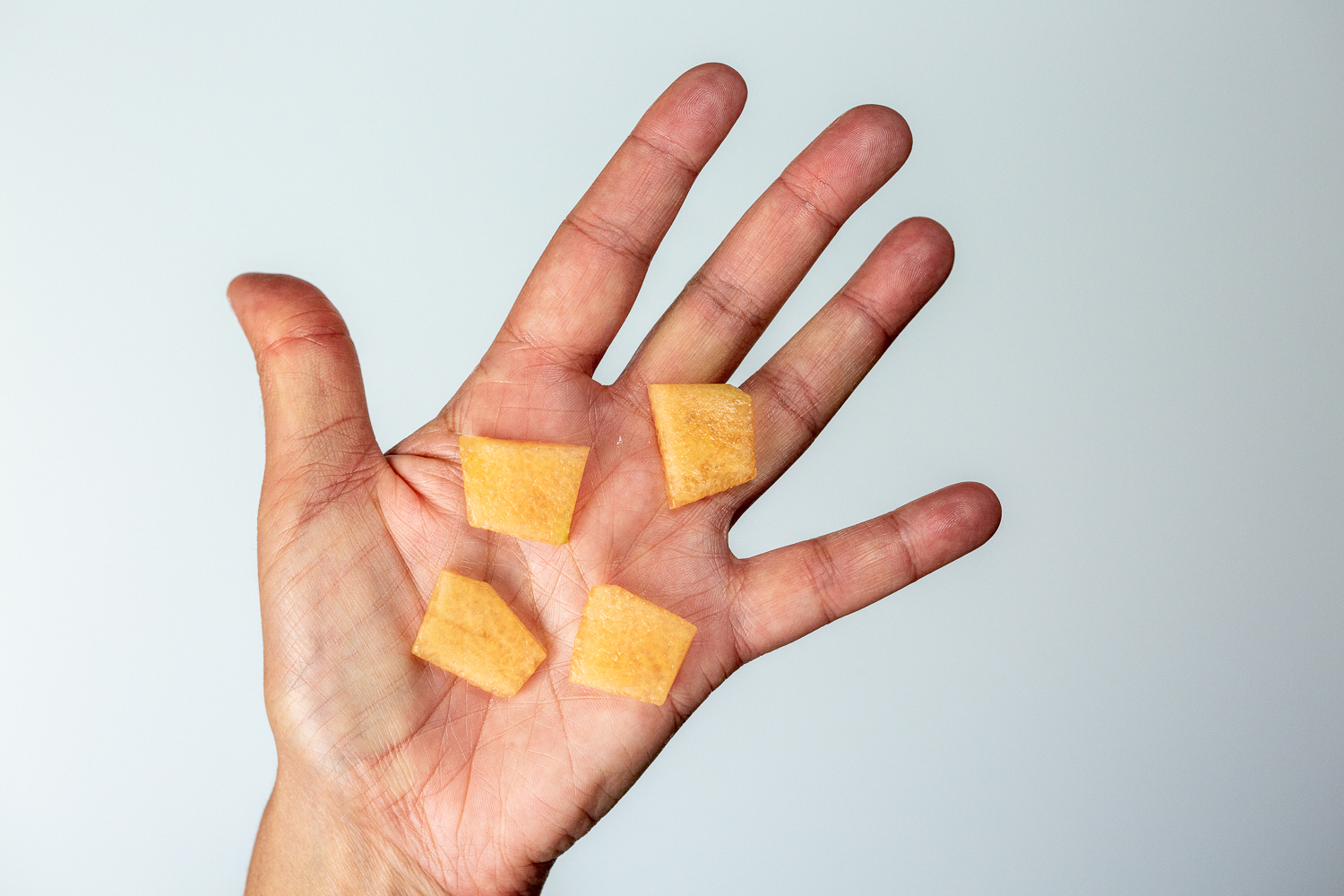 a hand holding four bite-sized pieces of cantaloupe cut from a thin slice