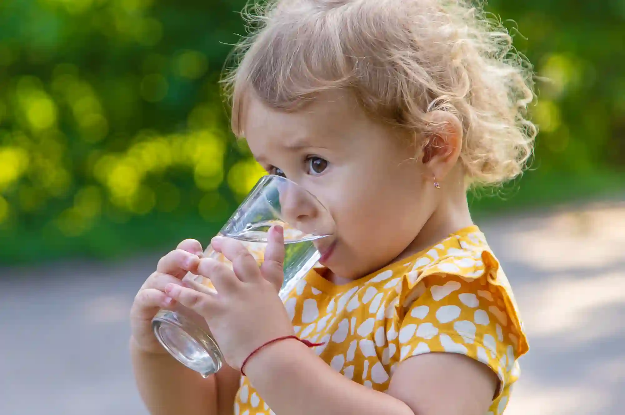a toddler standing outside and holding a glass with water in it to their mouth