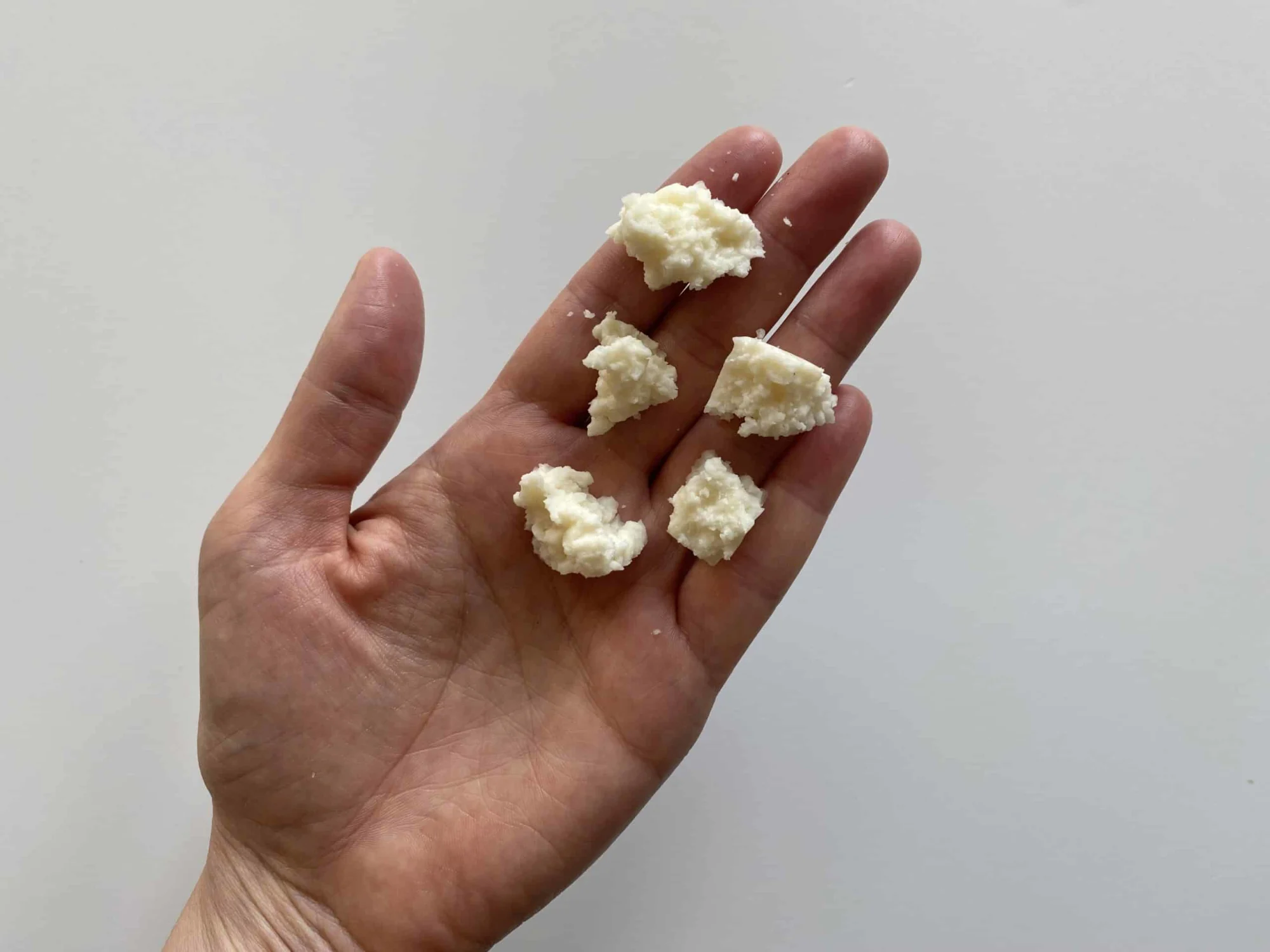 a hand holding five crumbles of cotija cheese