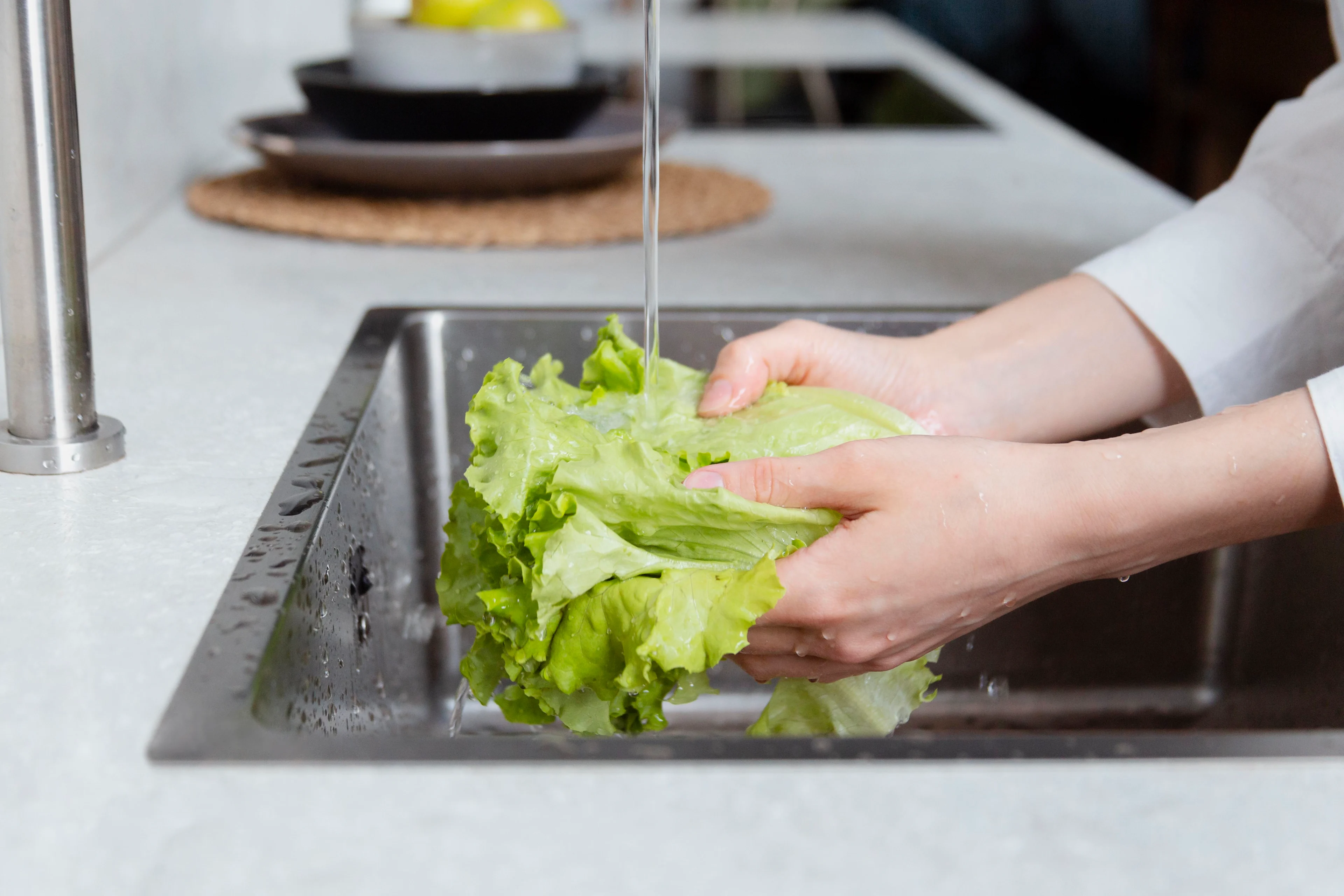 a photograph showing hands washing leaves of lettuce in a sink
