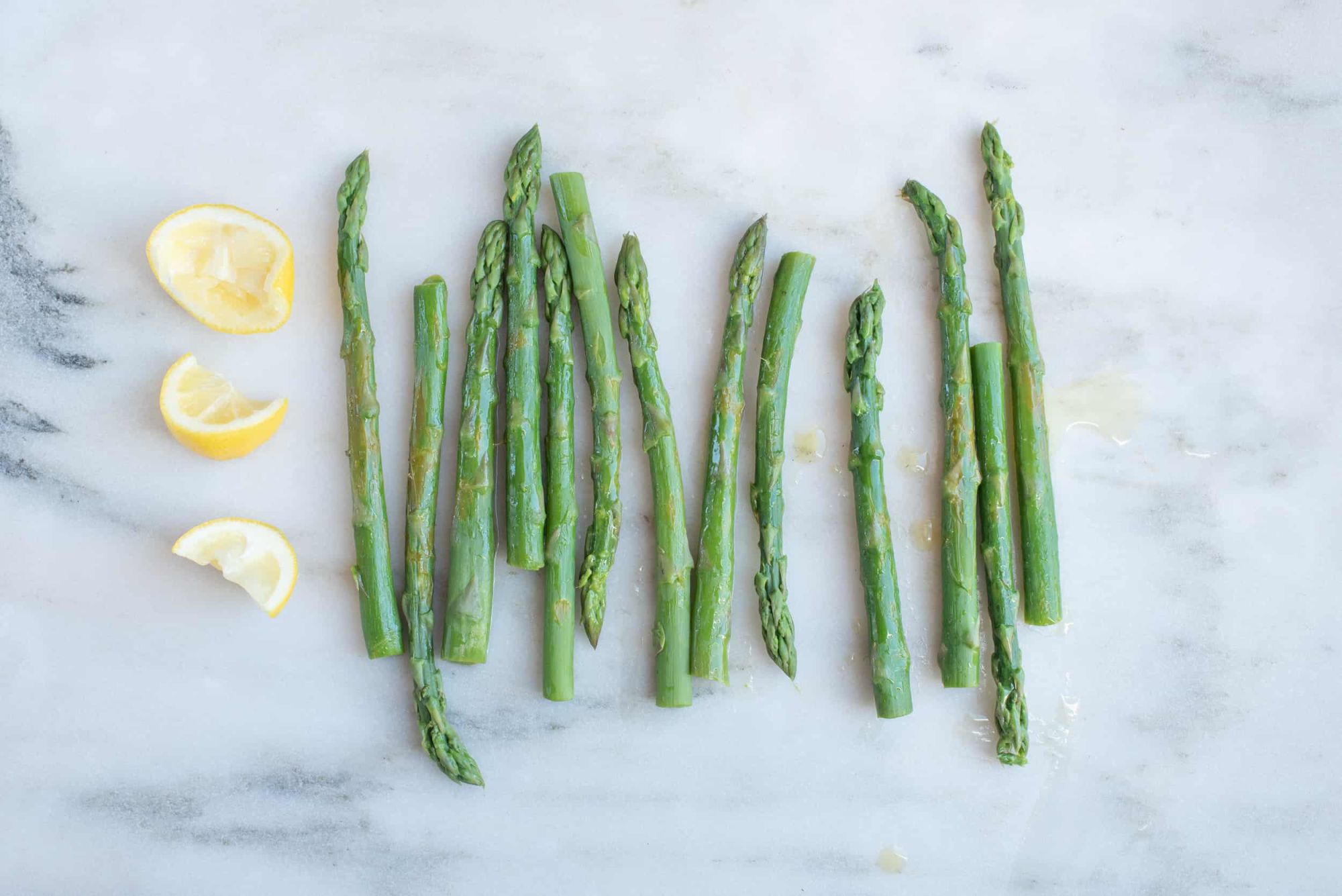 lemon wedges next to cooked whole asparagus spears on a white background