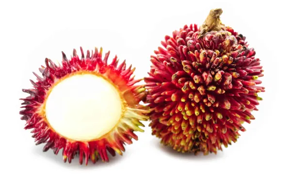 one whole pulasan next to one cut in half on a white background