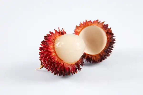one whole pulasan next to one cut in half on a white background