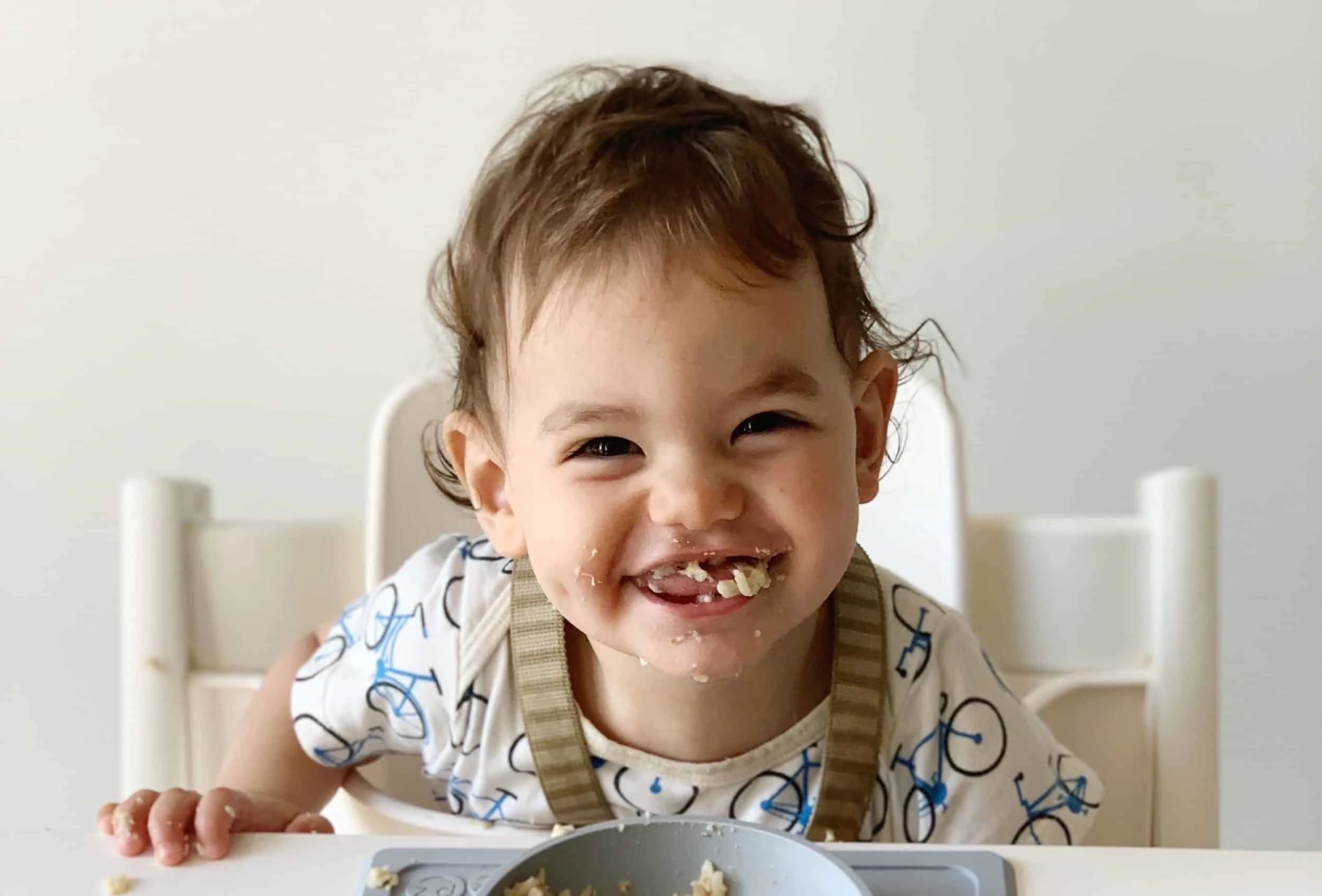 a baby smiling at the camera with food in his mouth