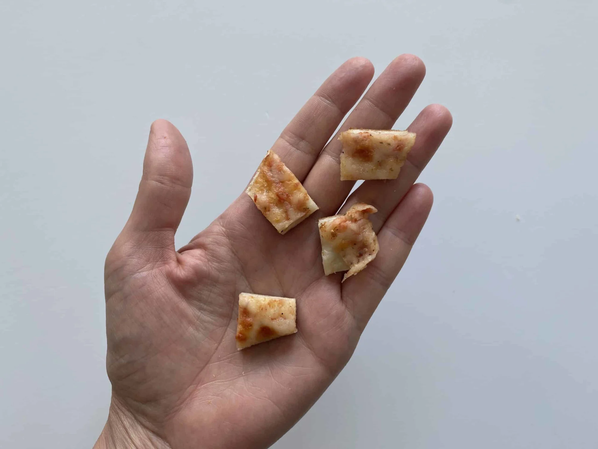 a hand holding four bite-sized pieces of cheese pizza for babies 9 months +