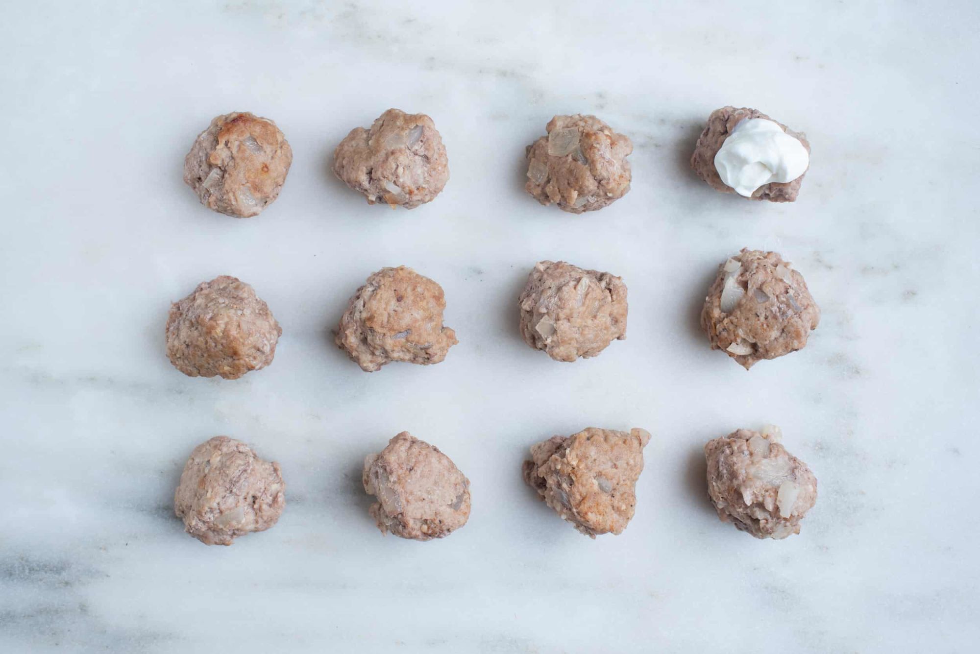 twelve turkey meatballs on a countertop, one of which is topped with Greek yogurt