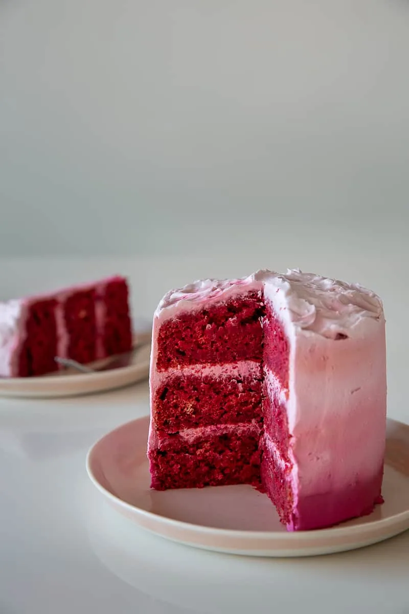 A cut apple beet cake reveals three deep-red layers with pink frosting between them.