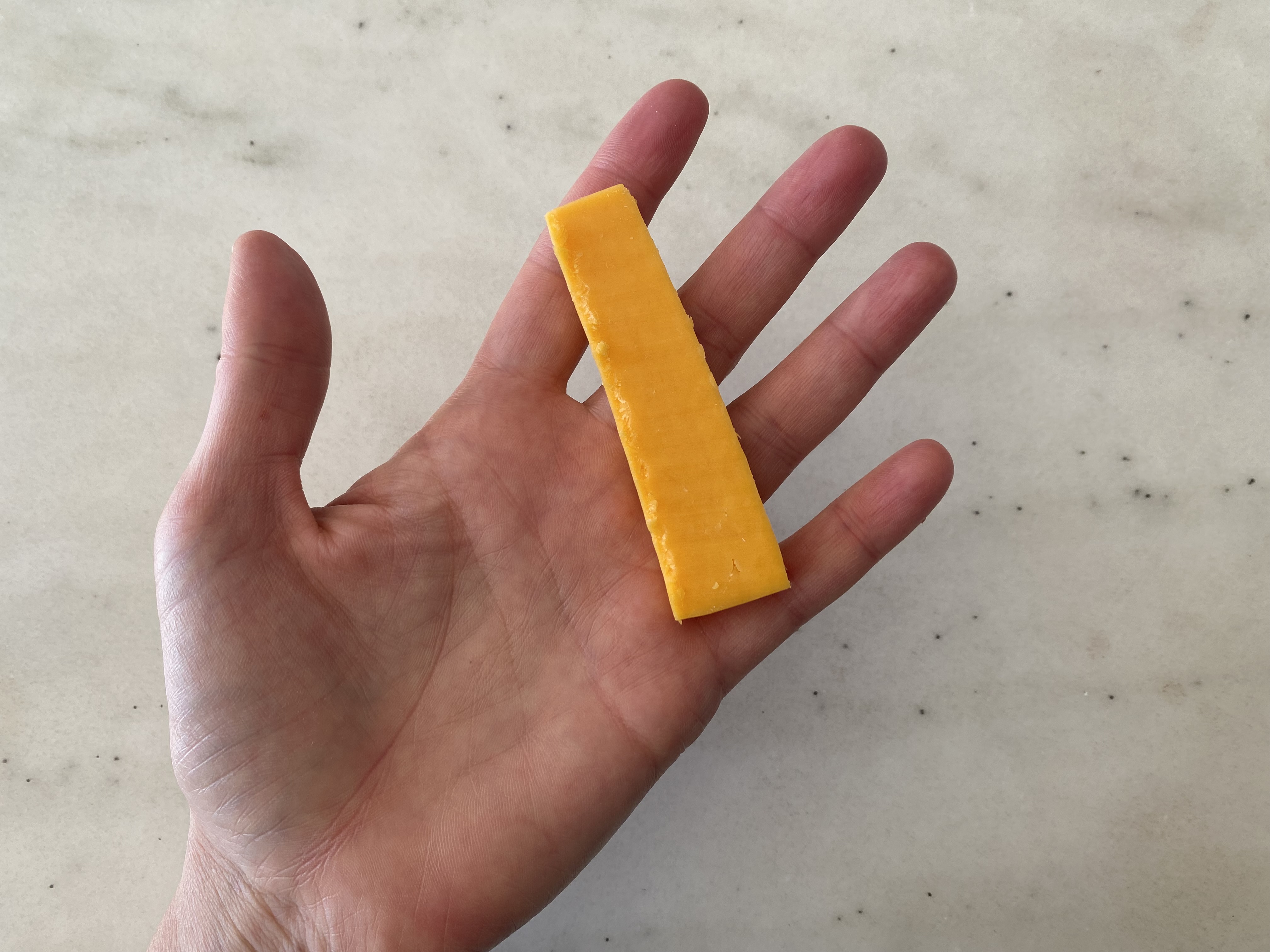 a hand holding a long, flat slice of orange cheddar cheese