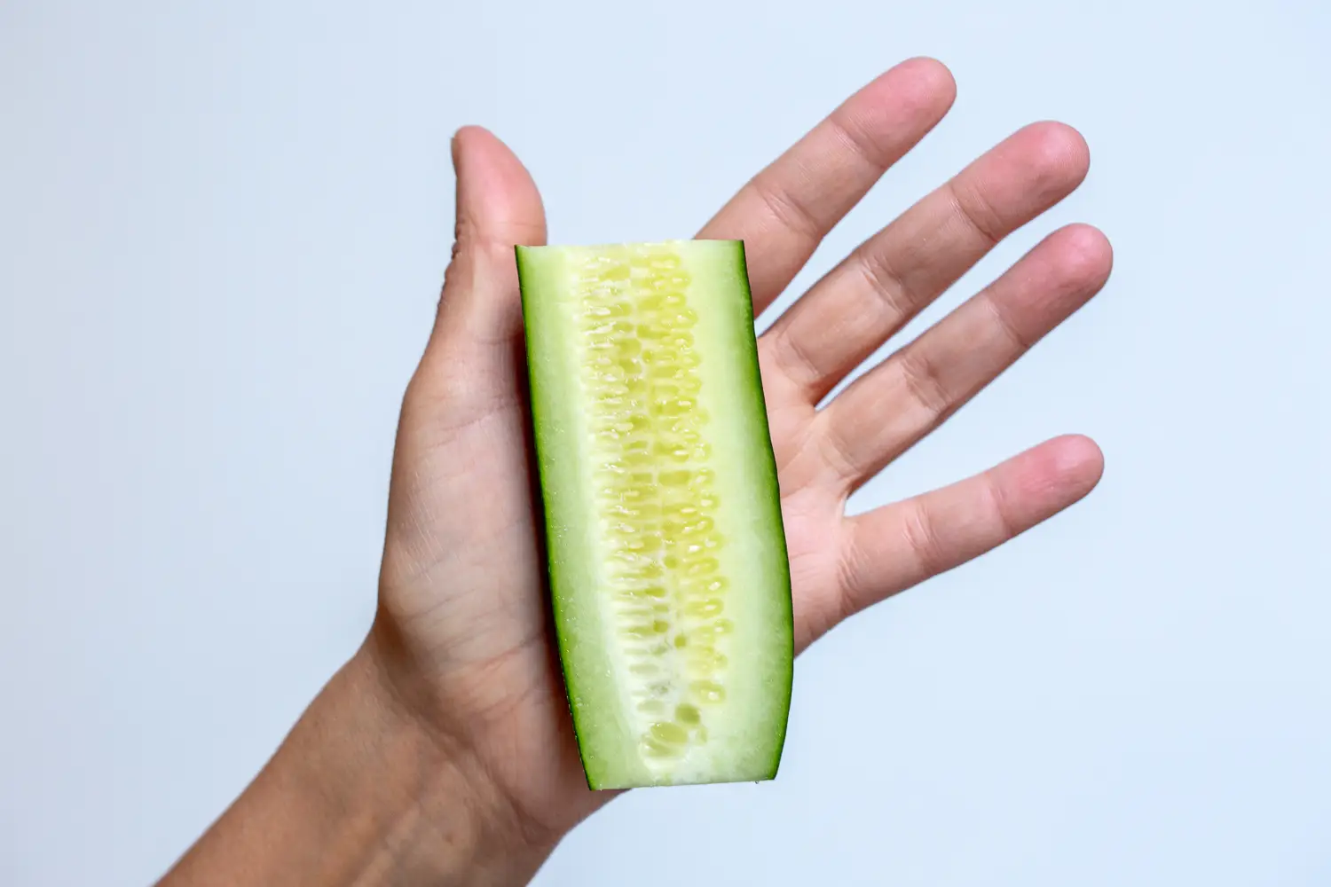a photograph of a hand holding a cucumber halved lengthwise