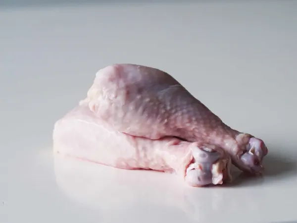a photograph of two raw chicken drumsticks ready to be cooked on a white background