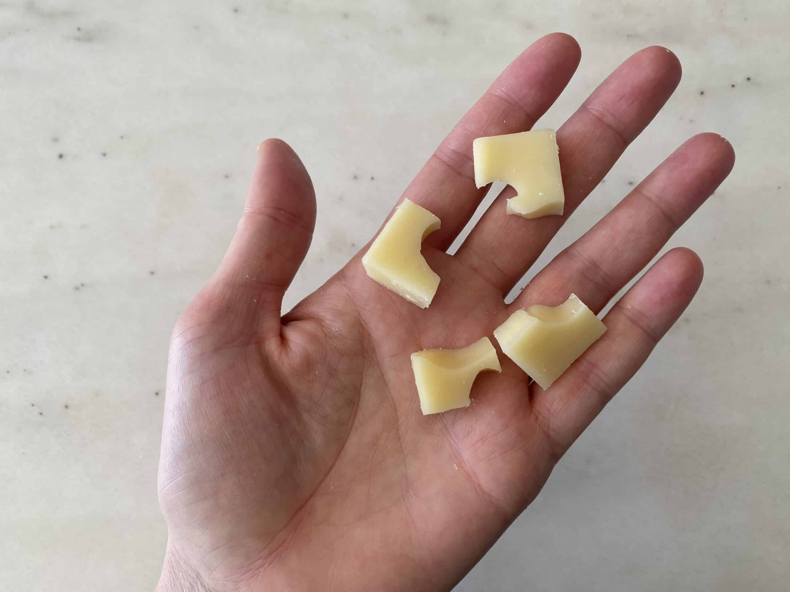 a hand holding four bite-sized pieces of swiss cheese for babies 9 months+