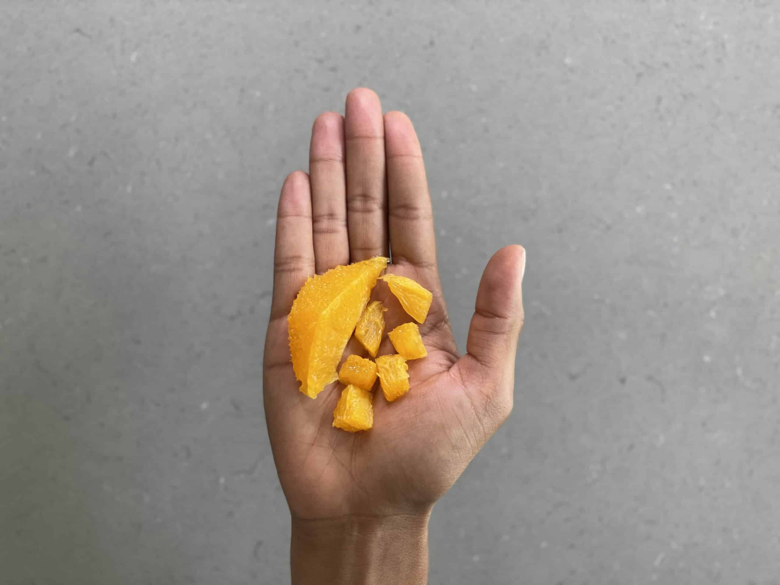 a hand holding one supremed orange wedge and small bite-sized pieces with the membrane removed