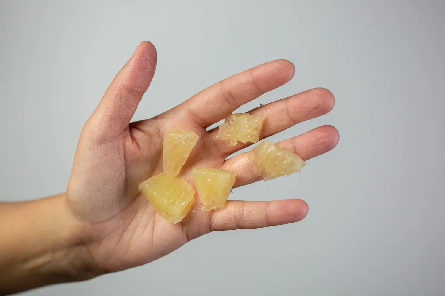 a hand holding five bite-sized pieces of peeled oroblanco, membrane removed, for babies 9 months+