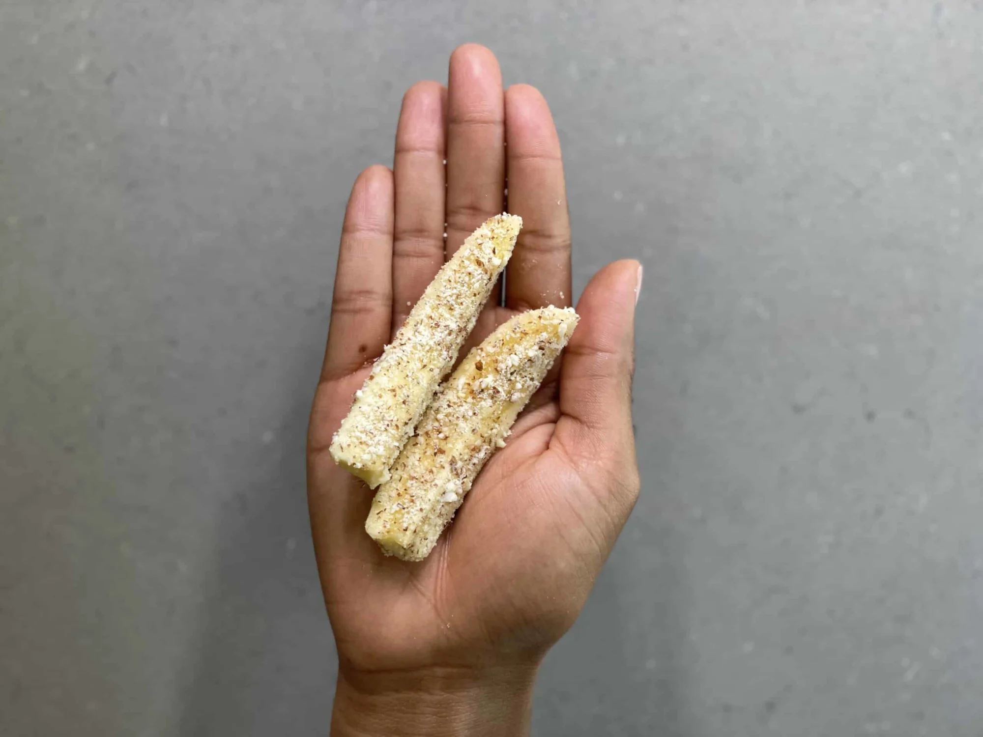 a hand holding two banana spears covered in finely ground almonds