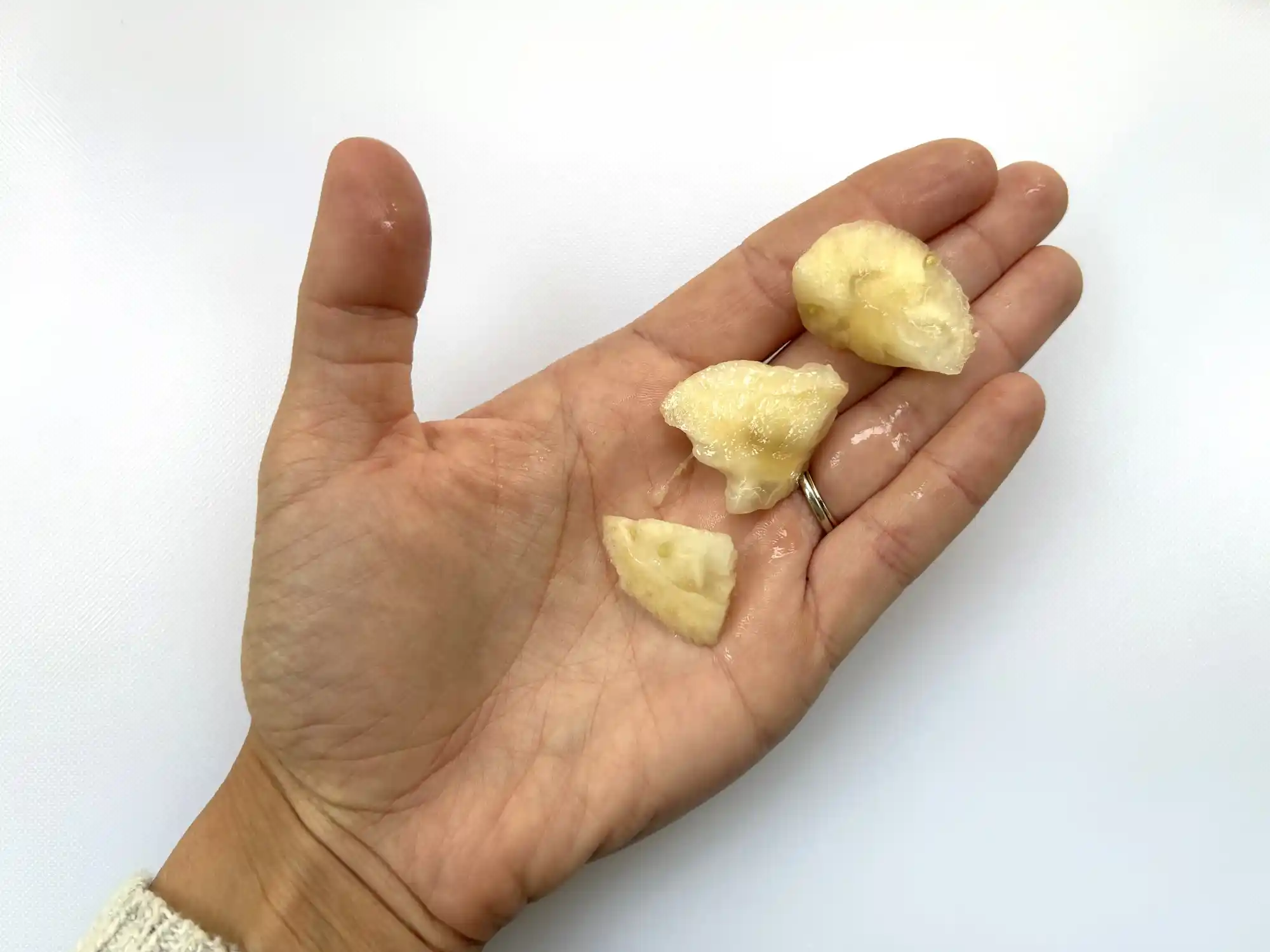 a photograph of a hand holding three bite-sized pieces of ripe feijoa
