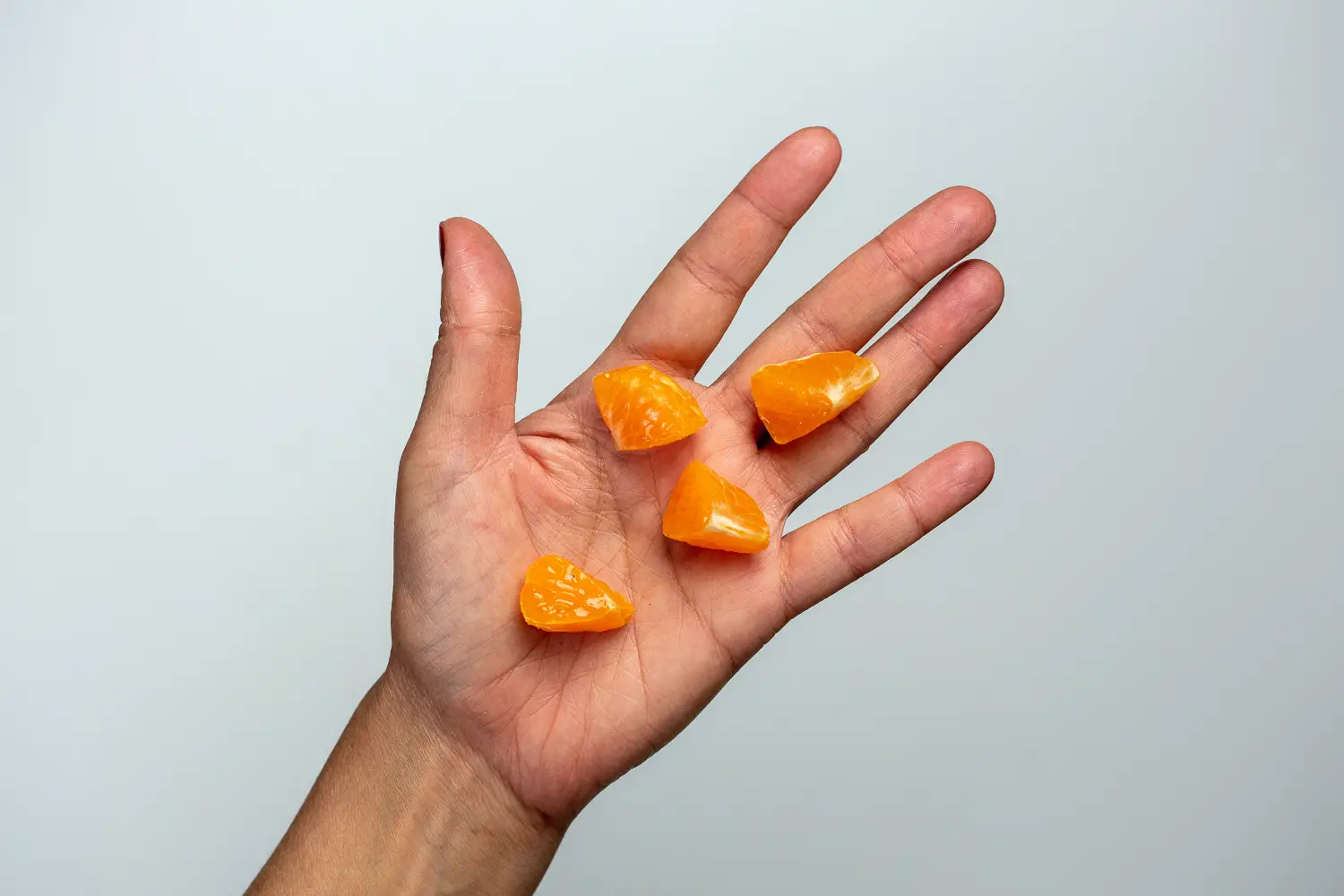 a hand holding four bite-sized pieces of clementine with membranes intact