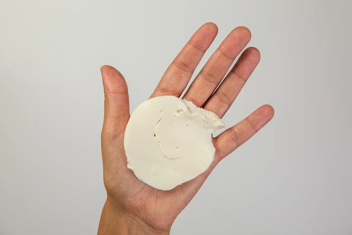 hand holding a large flat slice of mozzarella cheese