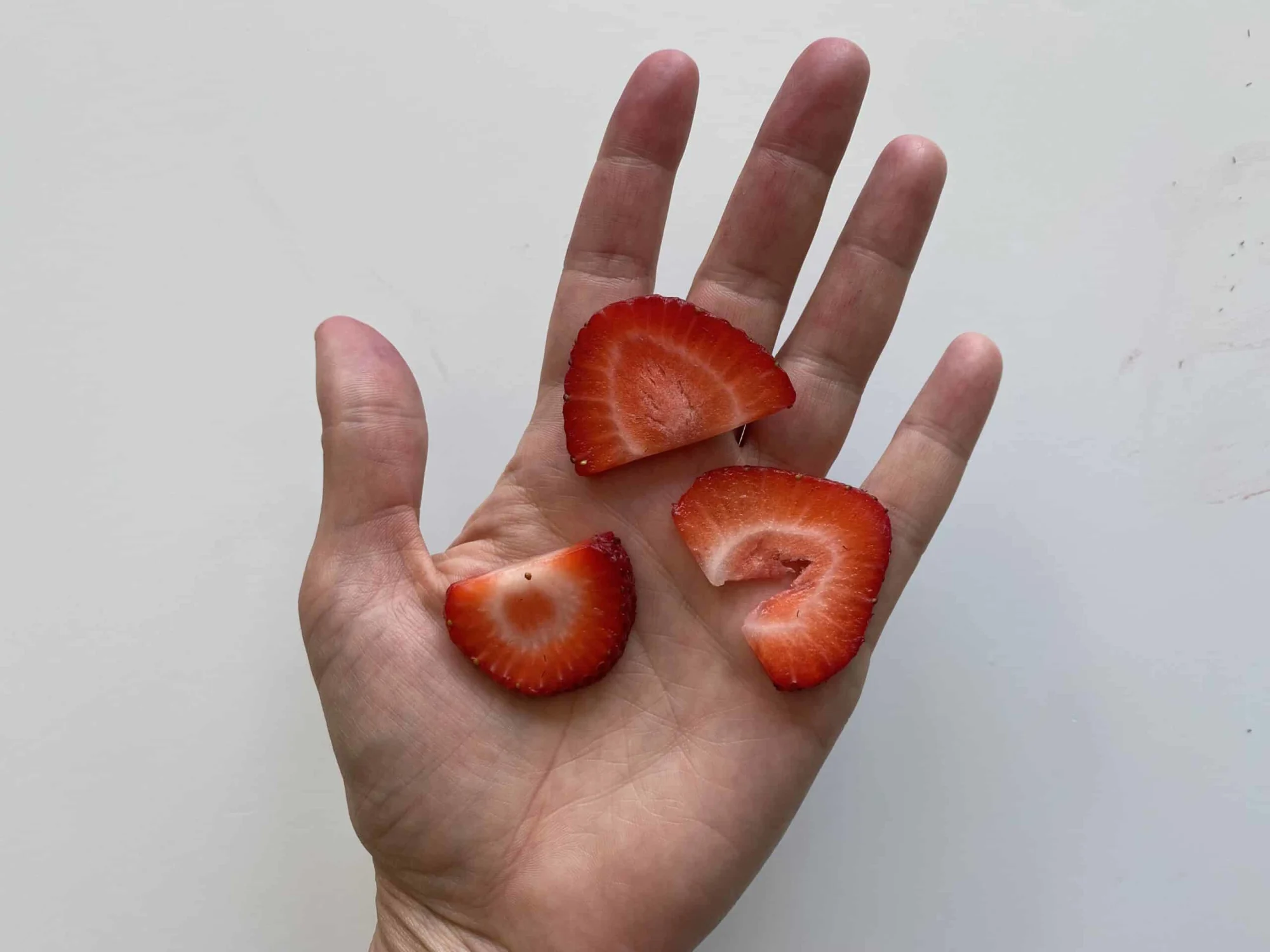 a hand holding three thin slices of strawberry for 9 months +