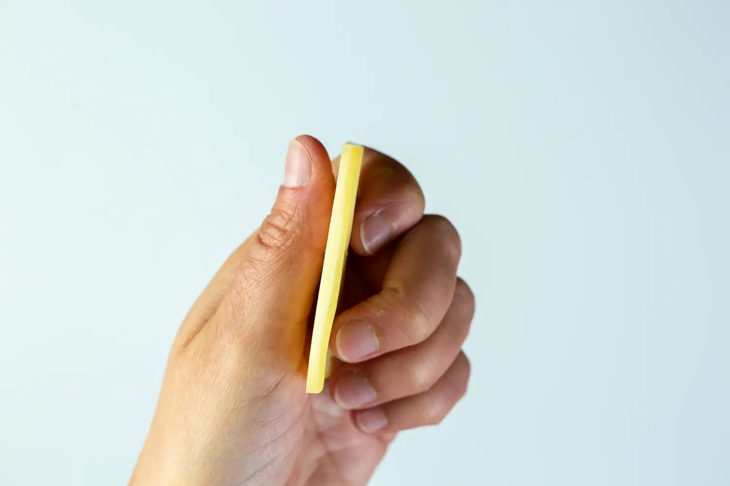 a photograph of a hand holding a flat slice of fontina to the side