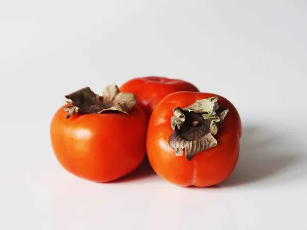 3 Fuyu persimmons on a white table before being prepared for babies starting solids