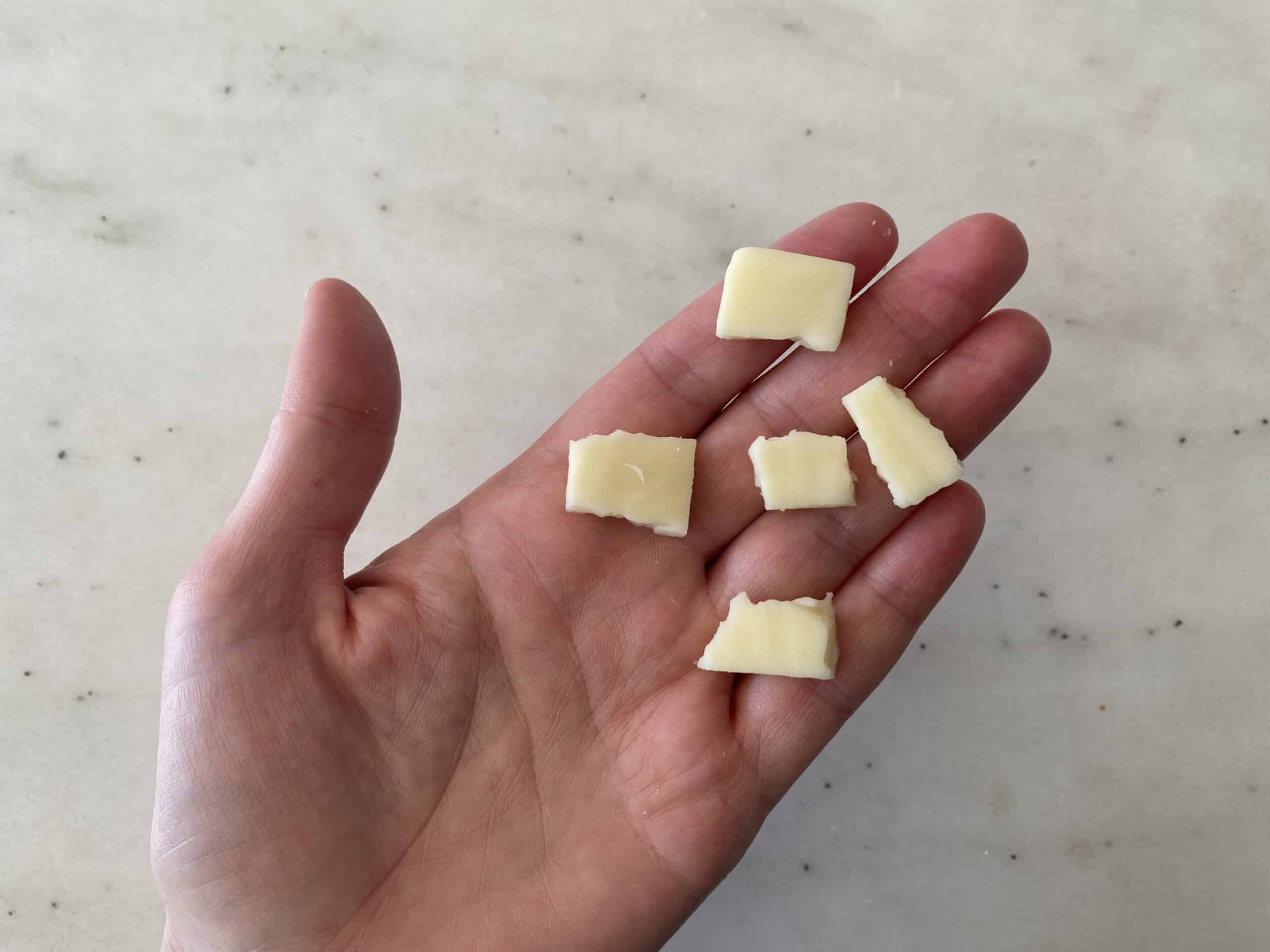 a hand holding five bite-sized pieces of monterey jack cheese for babies 9 months+