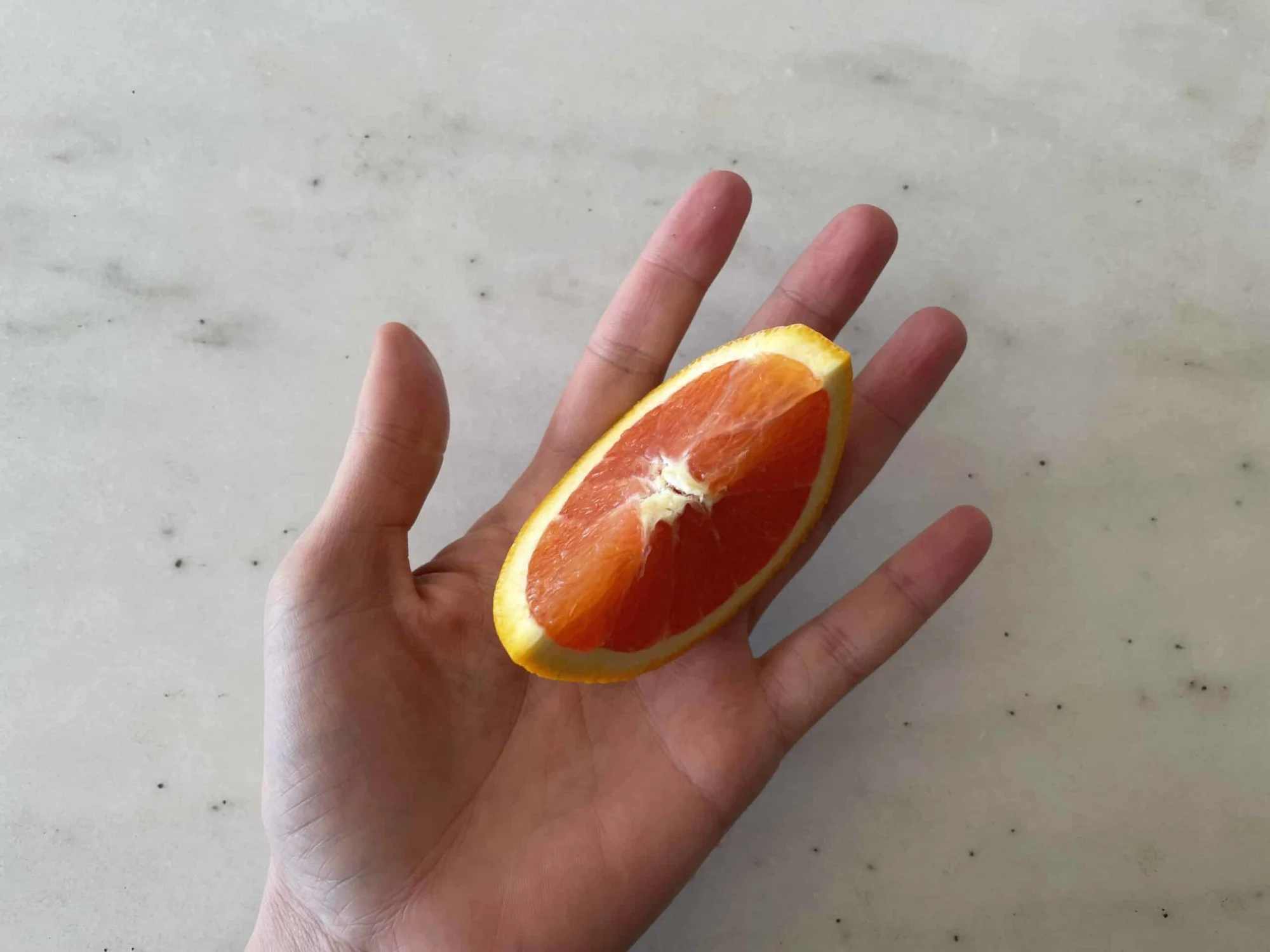 a hand holding an orange wedge with peel still on and seeds removed for babies 6 months+