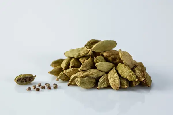a pile of whole cardamom pods next to one pod split open and nine cardamom seeds in front of it