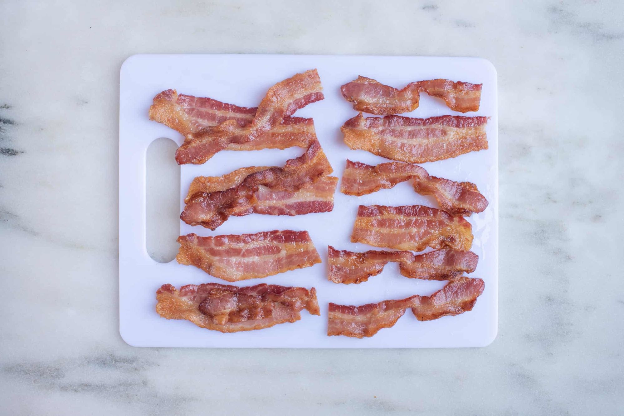 twelve pieces of baked short bacon strips on a white cutting board