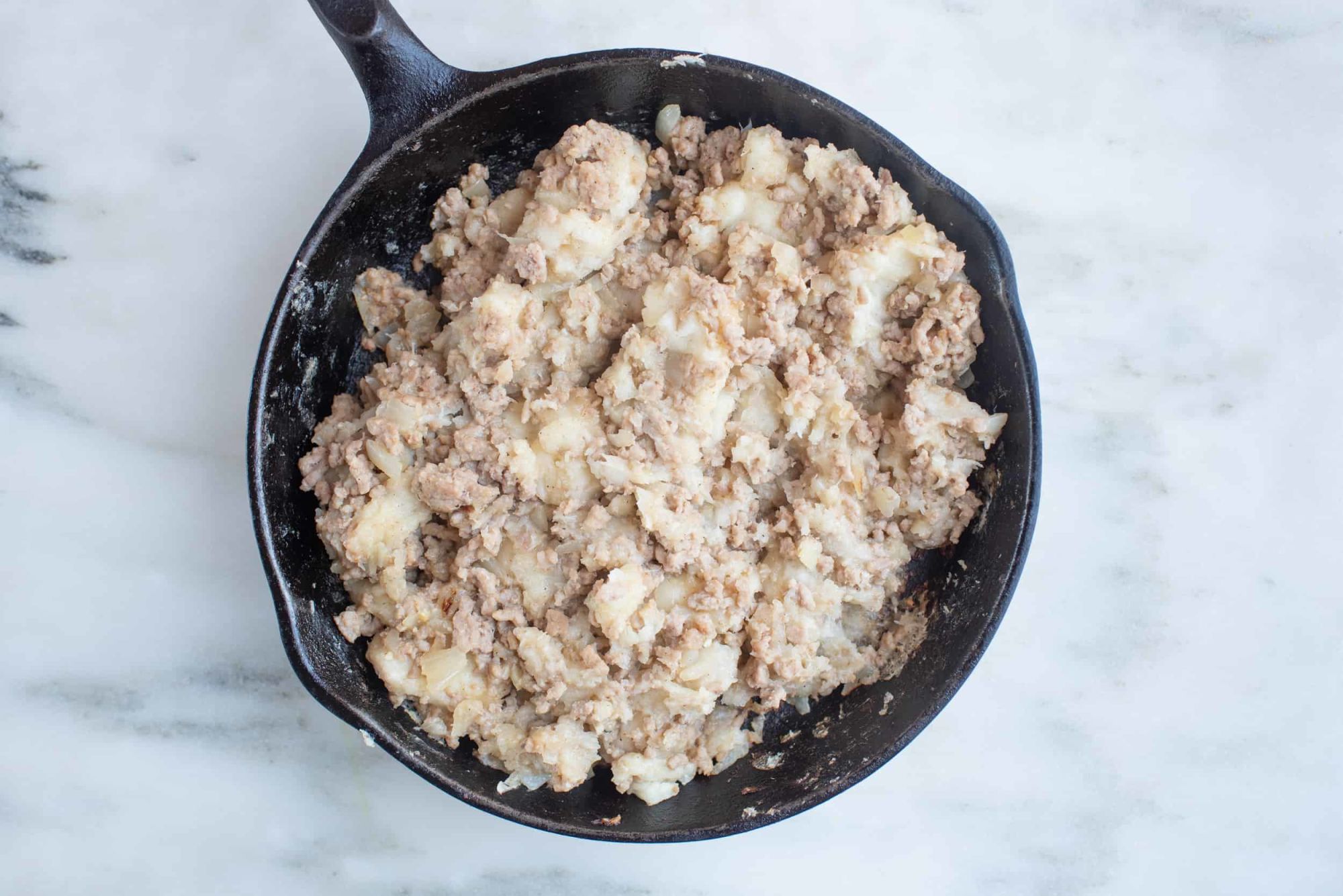 ground pork and mashed cooked cassava in a cast iron skillet