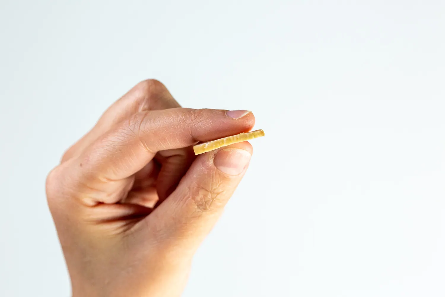 a photograph of a hand holding one thin slice of cooked chestnut between the thumb and pointer finger