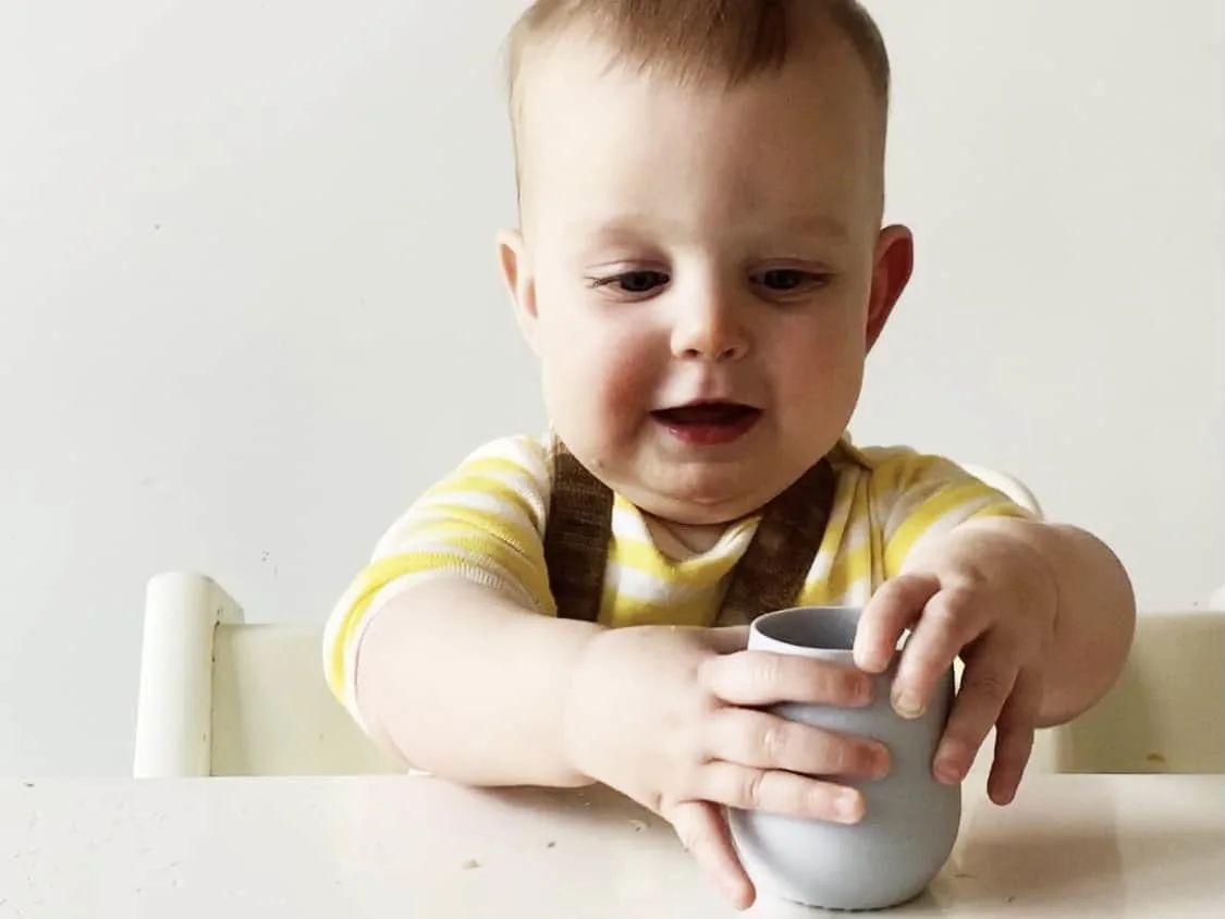 A 7 month old baby holding an open cup