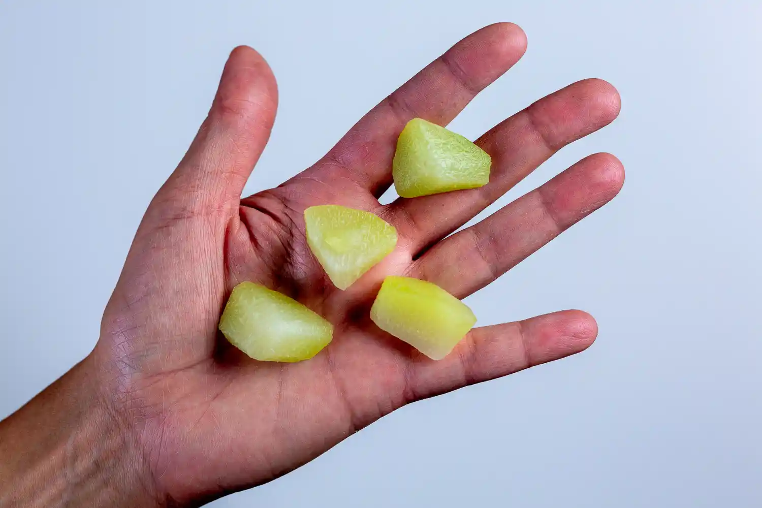 a photograph of a hand holding four bite-sized pieces of cooked chayote in the palm