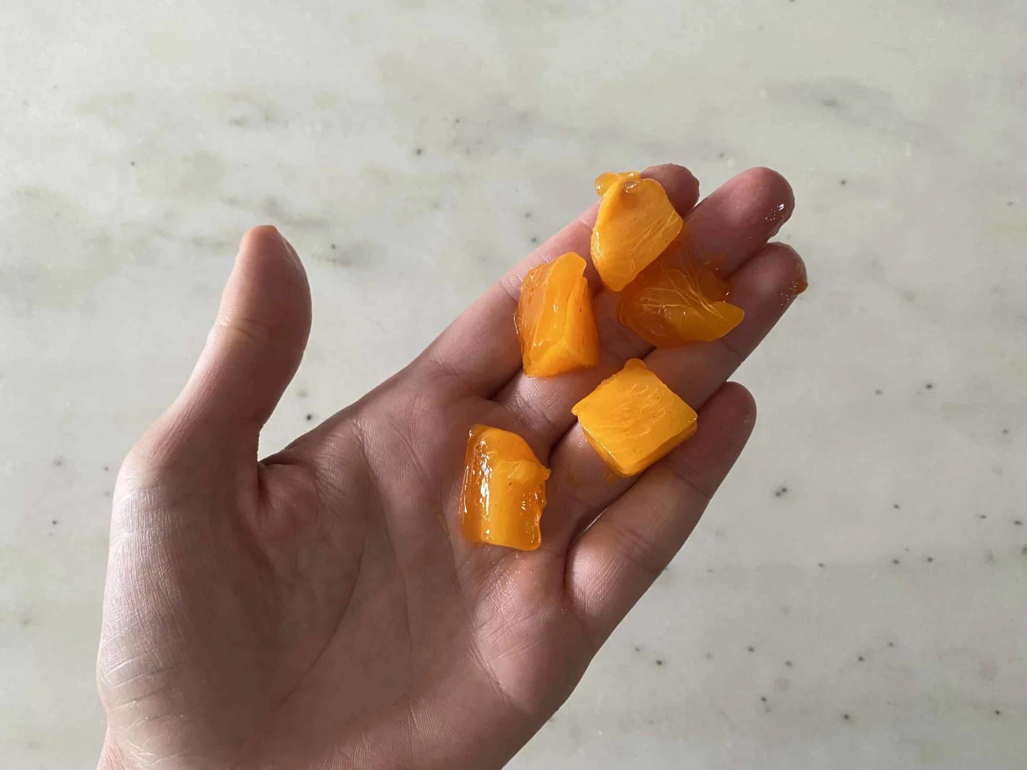 a hand holding five bite sized pieces of ripe, soft Hachiya persimmon for children 12 months +