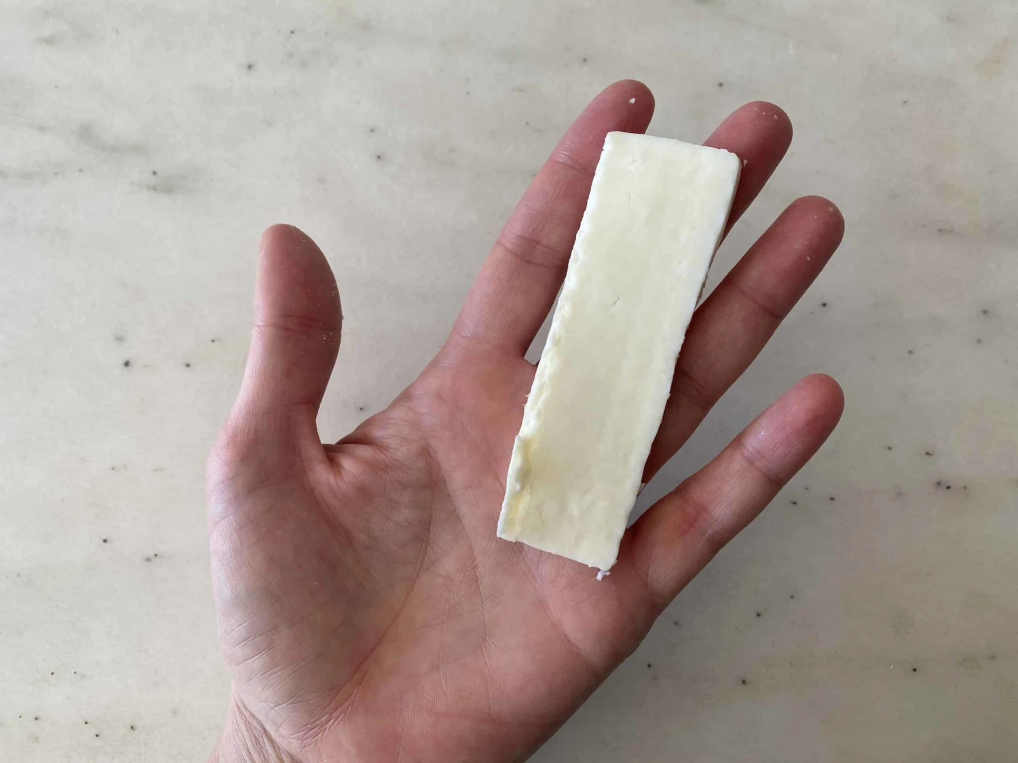 a hand holding a thin slice of paneer for babies 6 months+