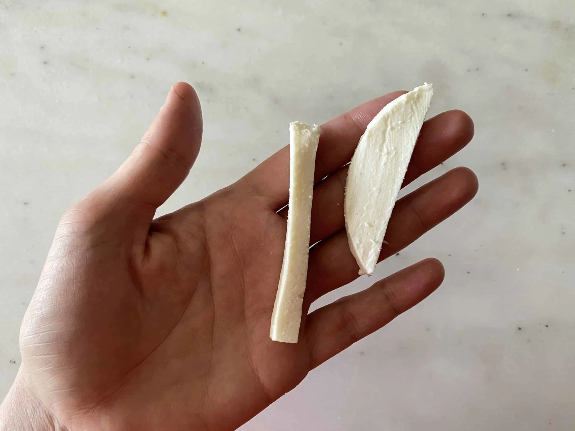 hand holding two thin strips of mozzarella cheese