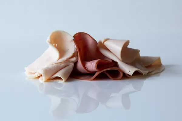 a photograph of a few pieces of deli meat on a reflective white background