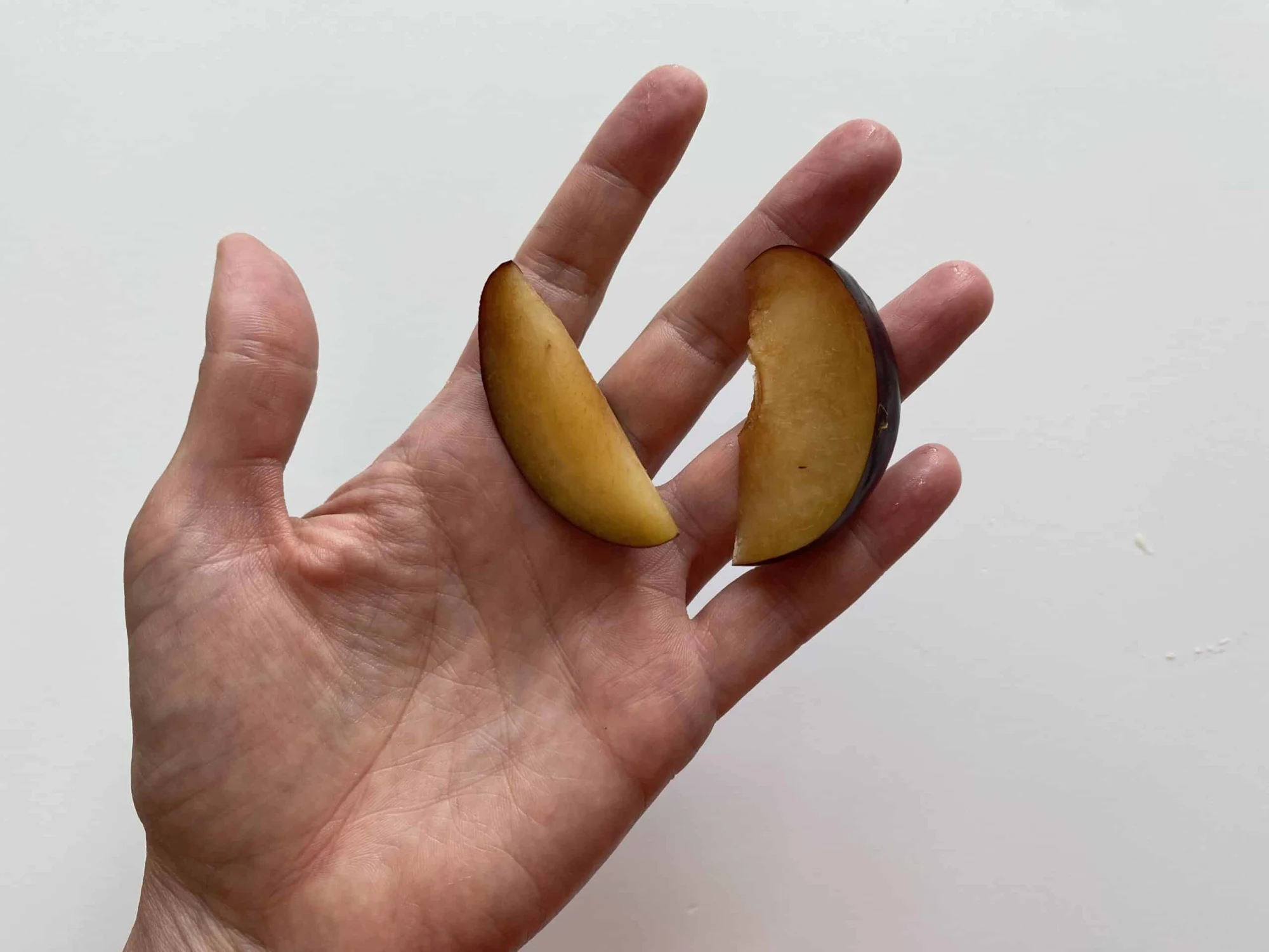 a hand holding two slices of plum for babies 9 months +