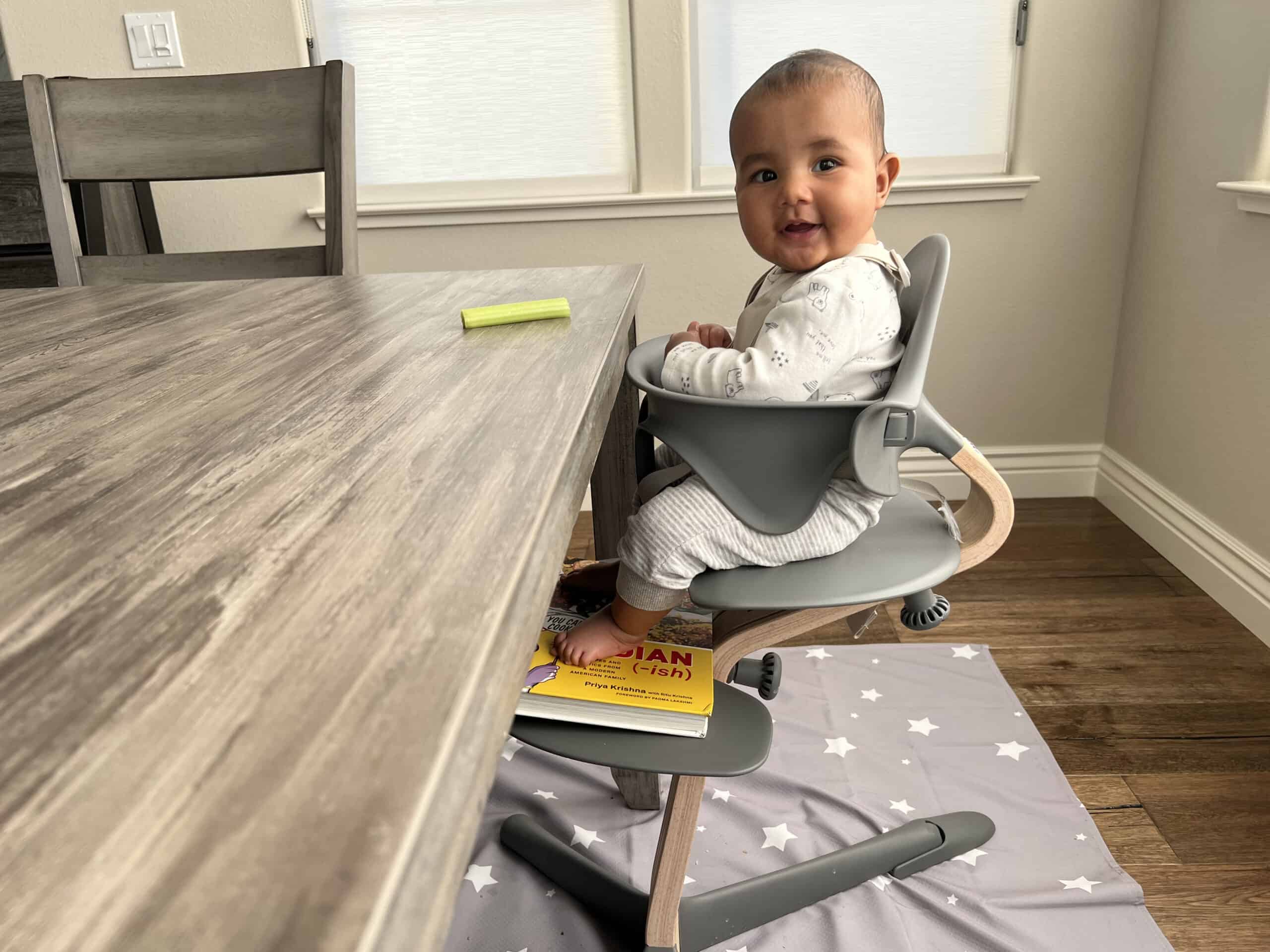 baby sits in high chair with a book under her feet