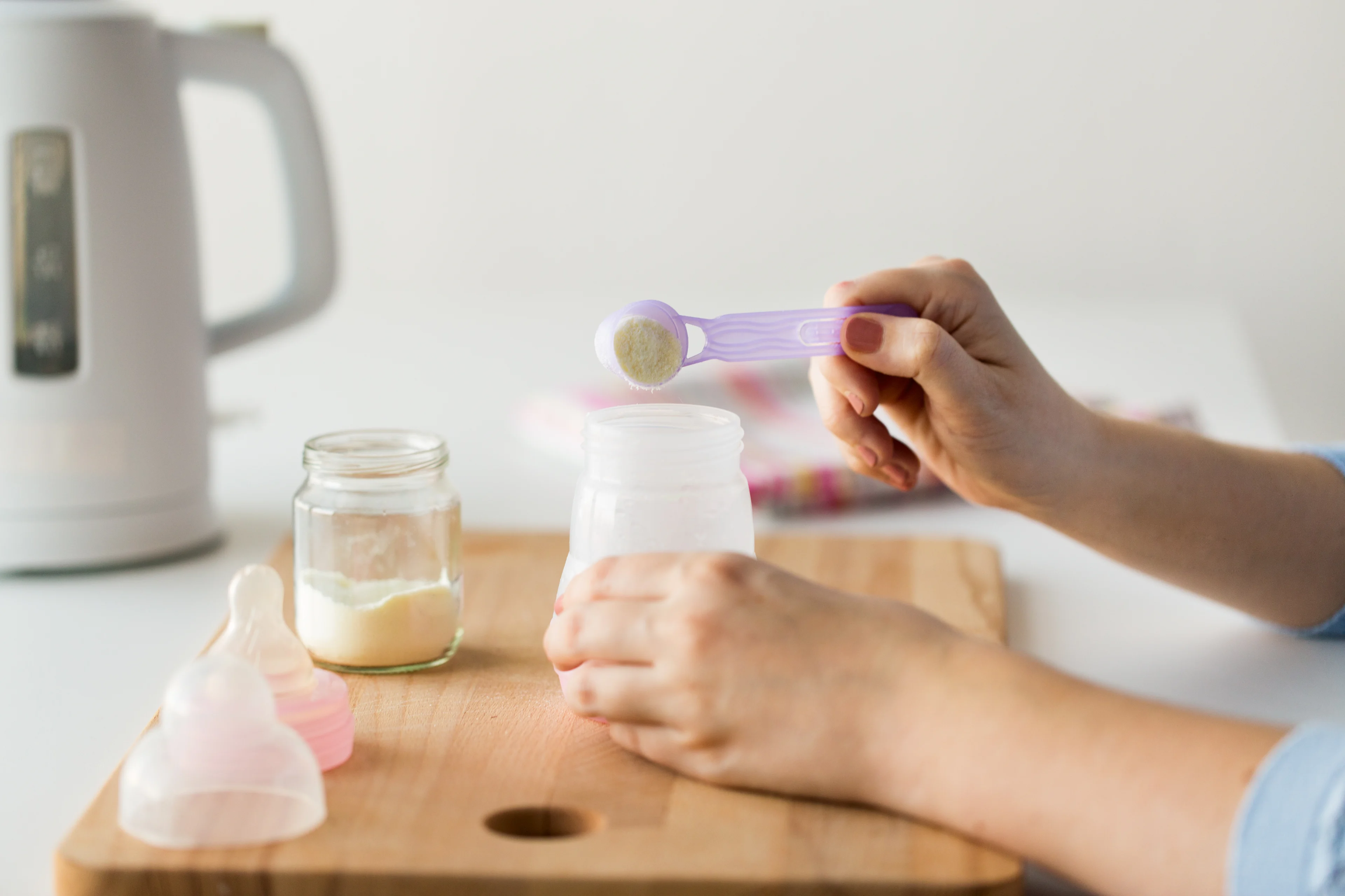 a photograph close up of hands preparing a bottle of infant formula using powder