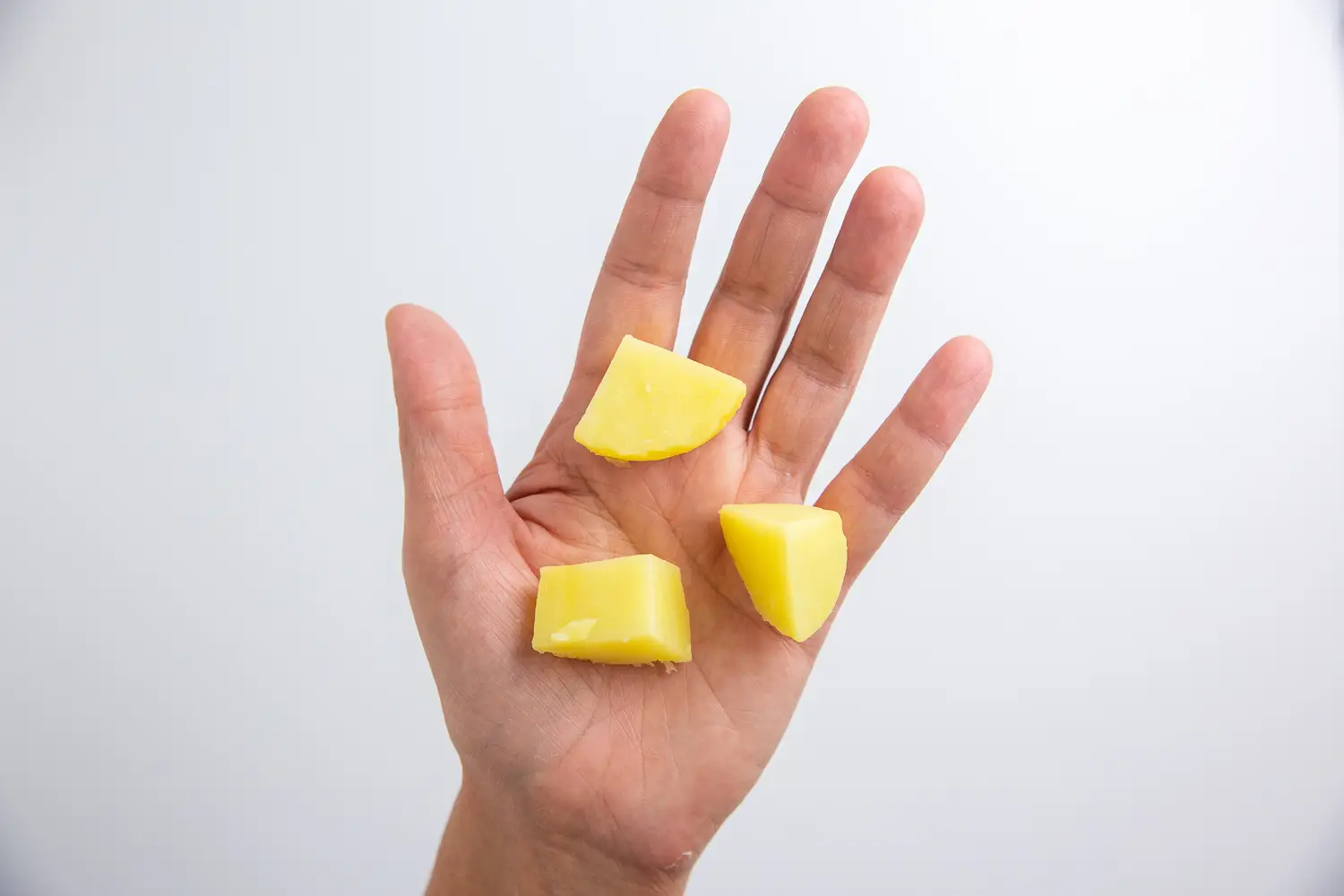 a photograph of a hand holding out three bite sized pieces of white potato