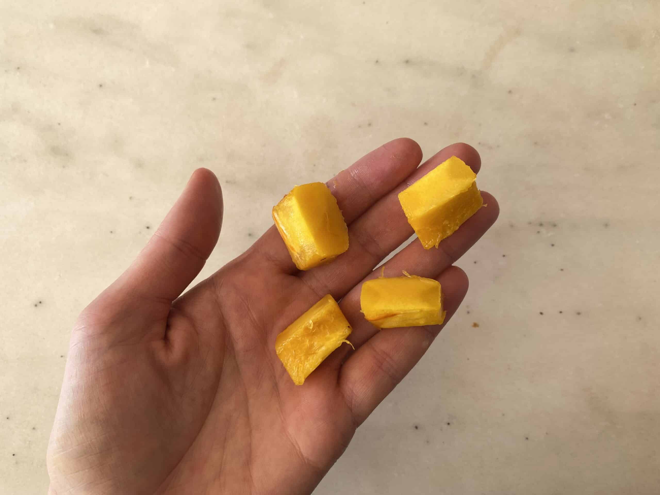 a hand holding four bite-sized pieces of cooked delicata squash for babies starting solids