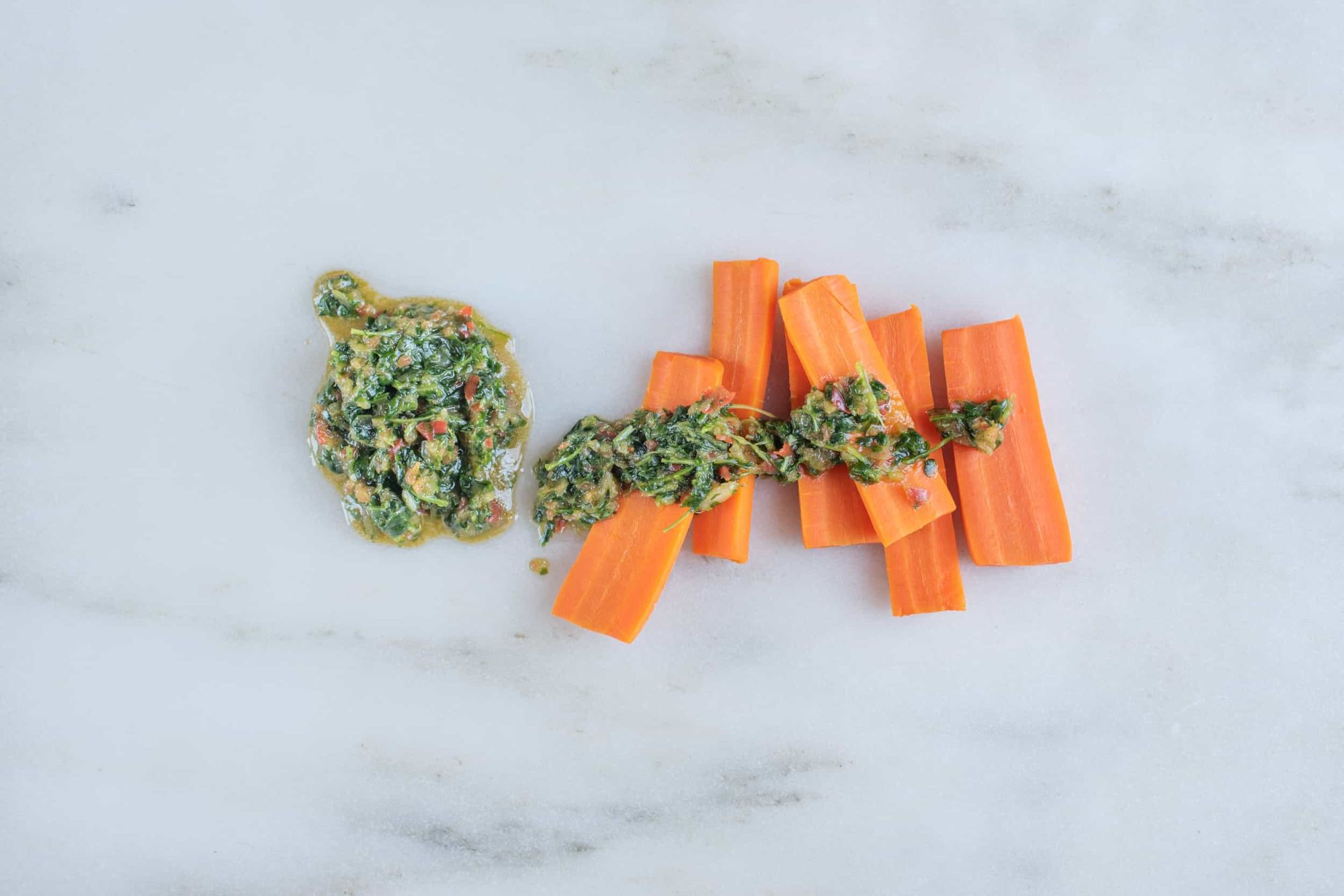 six cooked carrot sticks with cilantro and pepper sauce drizzled on top on a white background