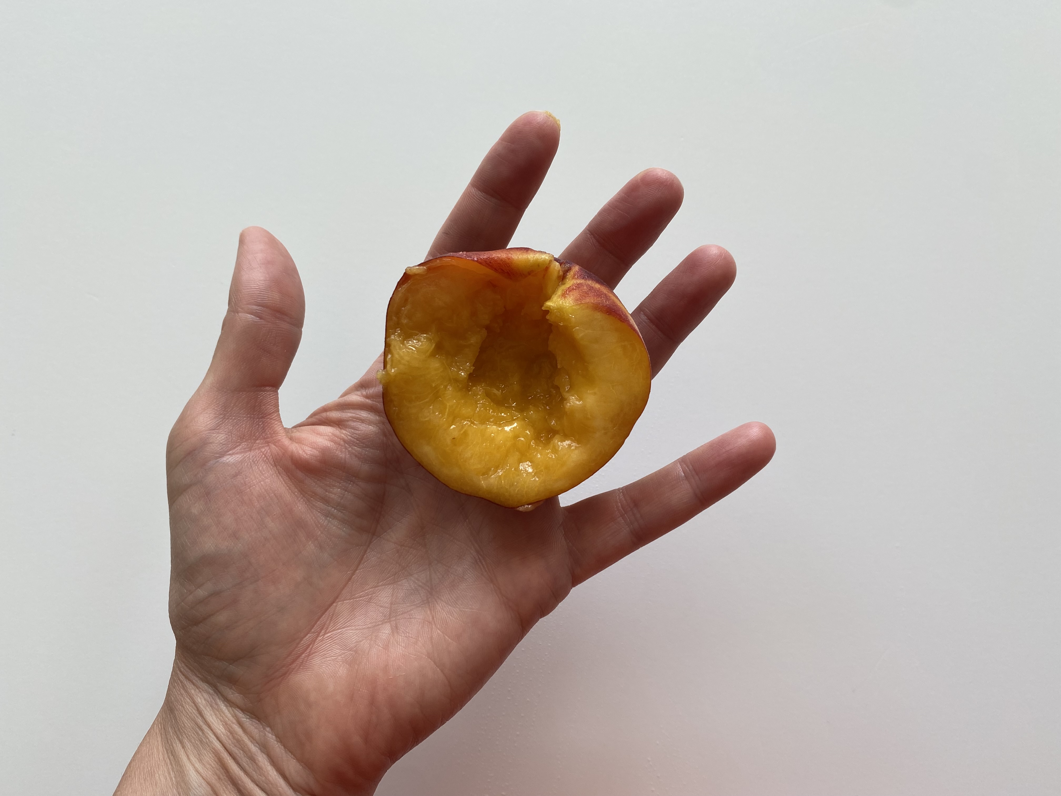 a hand holding a ripe half of a peach with the pit removed and the skin still on