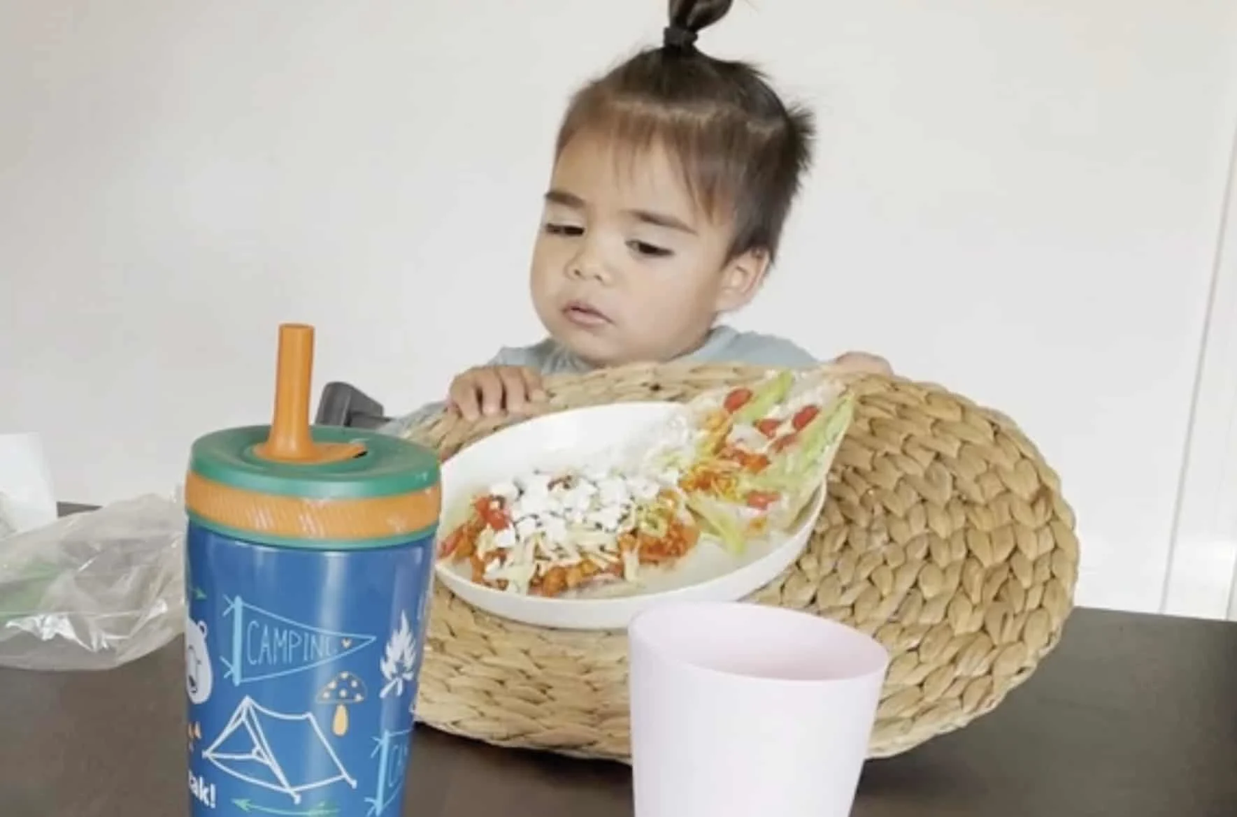 un niño pequeño sentado a la mesa empujando un individual con un plato de comida 
