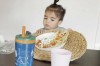 toddler sitting at the table pushing away a place mat with a plate with food on top